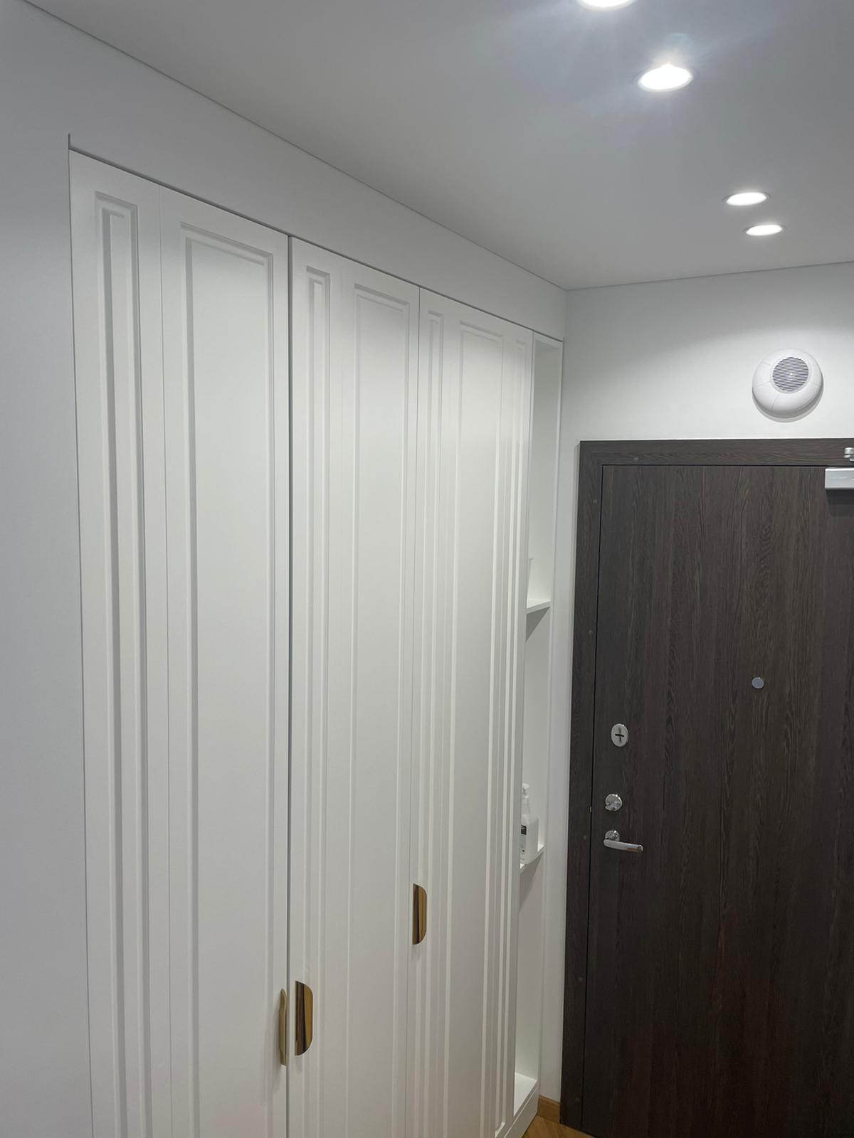 Prieškambaris su baltomis spintelėmis ir medinėmis durimis.