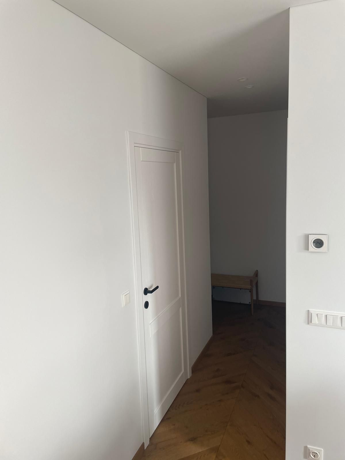 Koridorius su baltomis durimis ir medinėmis grindimis.