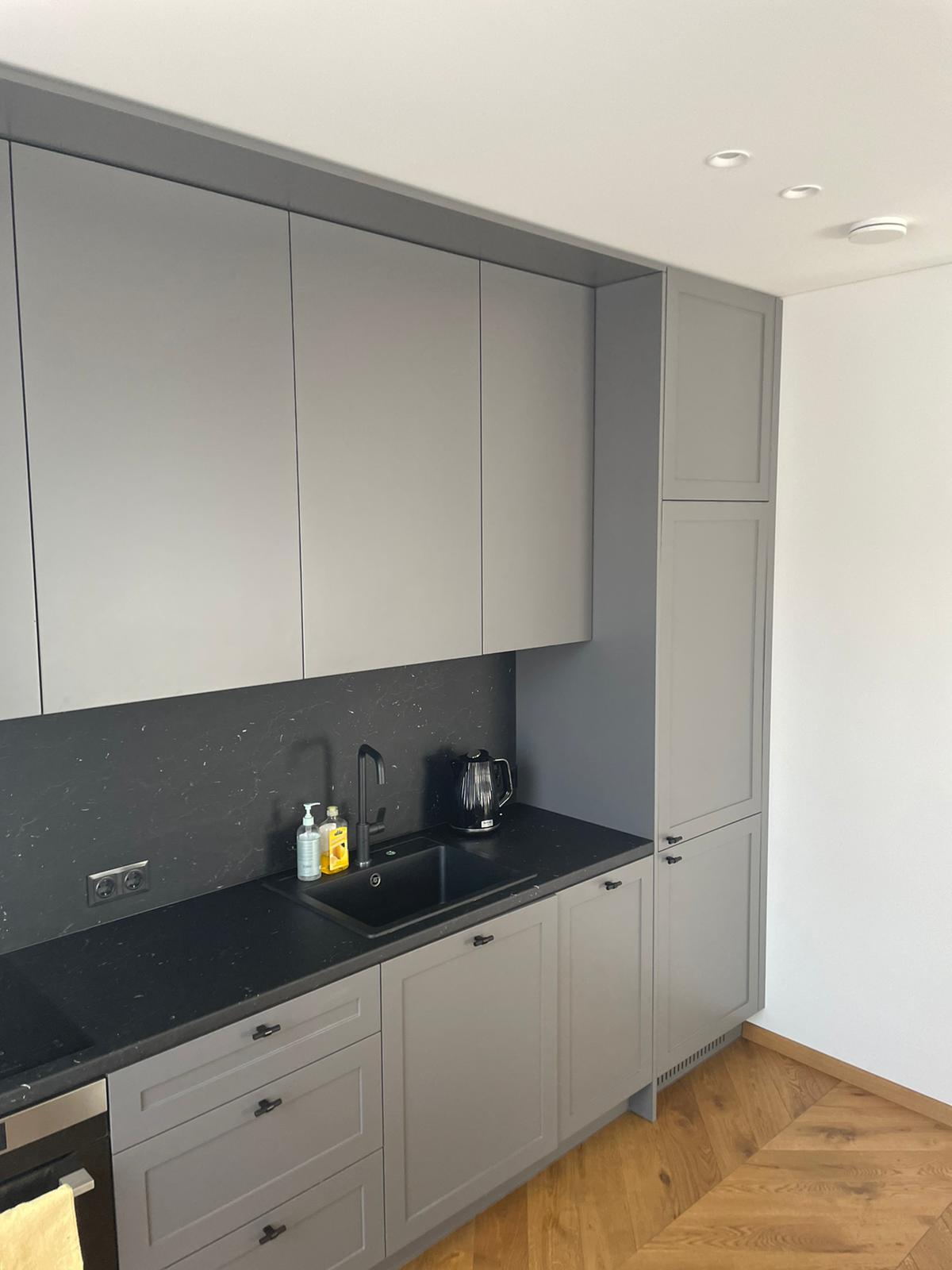 Virtuvė su pilkomis spintelėmis ir juodais stalviršiais