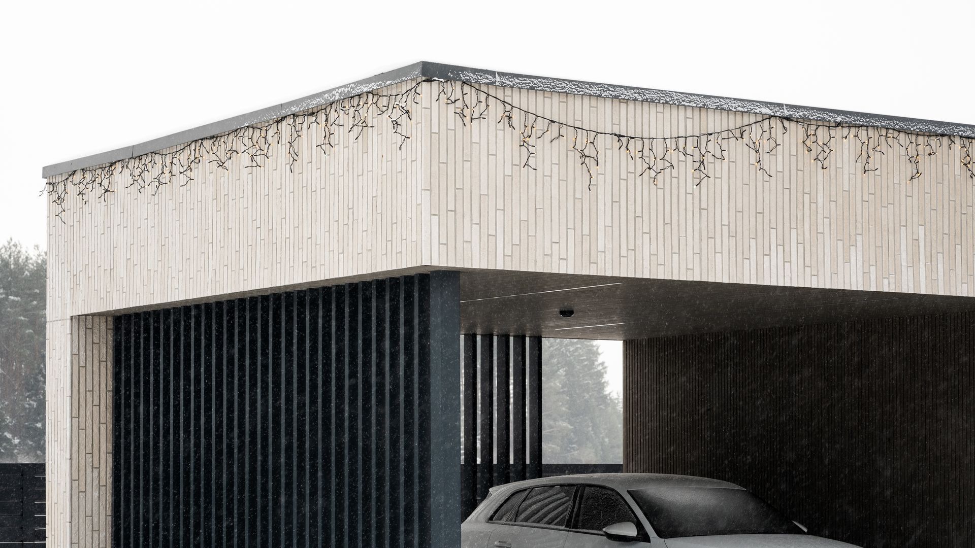 Modern car port with concrete and wooden slats; car sheltered inside during snowfall.