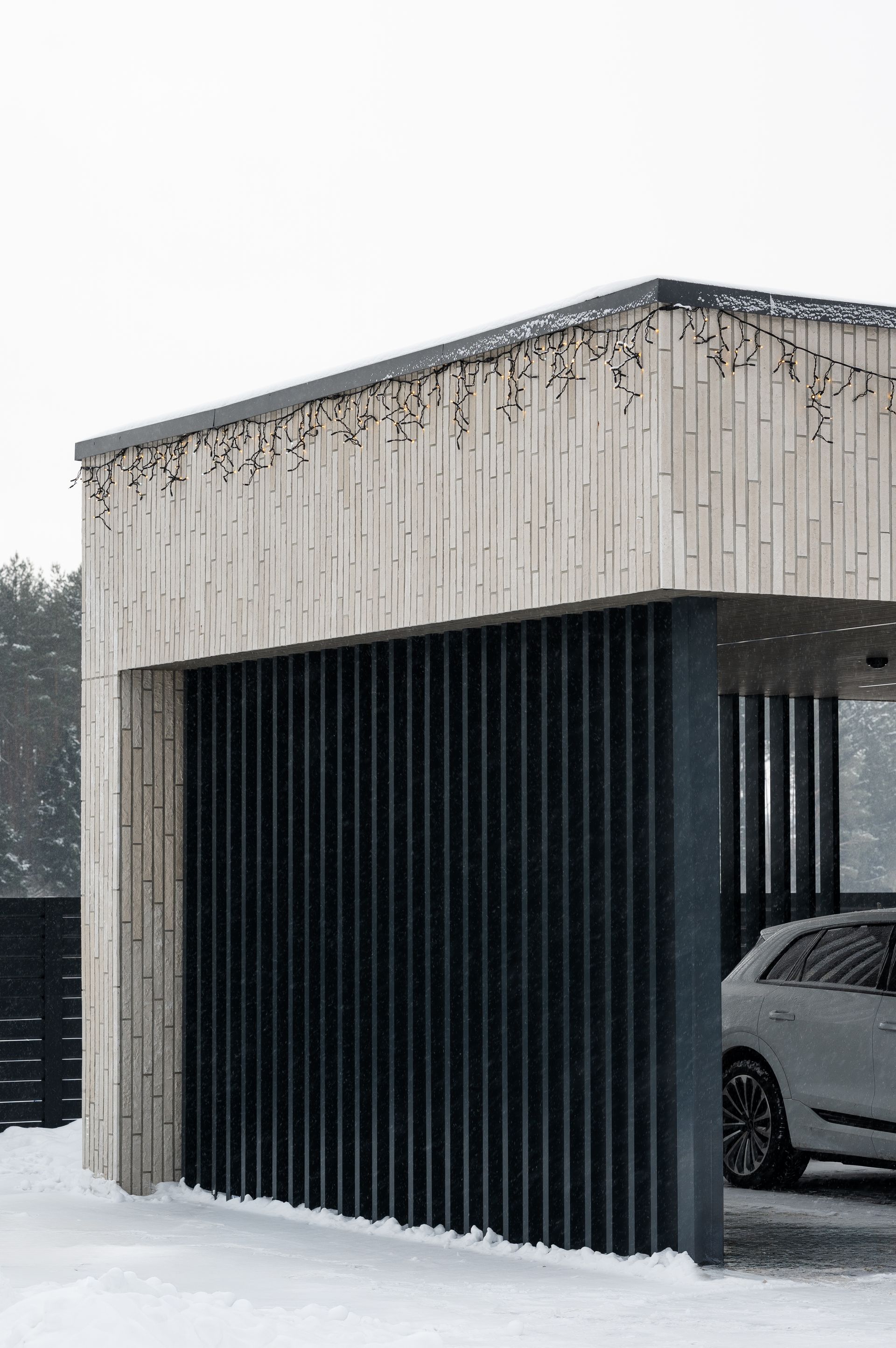 Car shelter with vertical black slats, snow falling, and a white SUV parked inside.