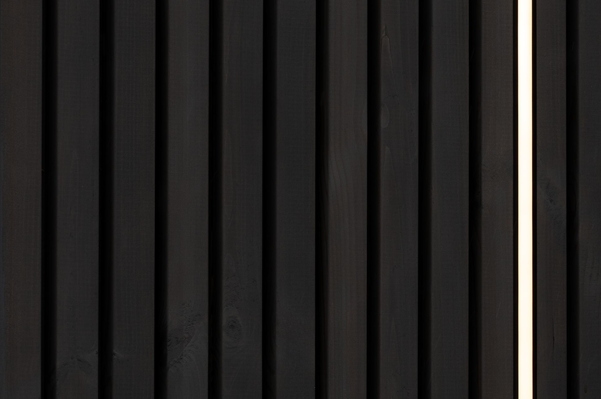 Black vertical wood paneling with a narrow illuminated strip.