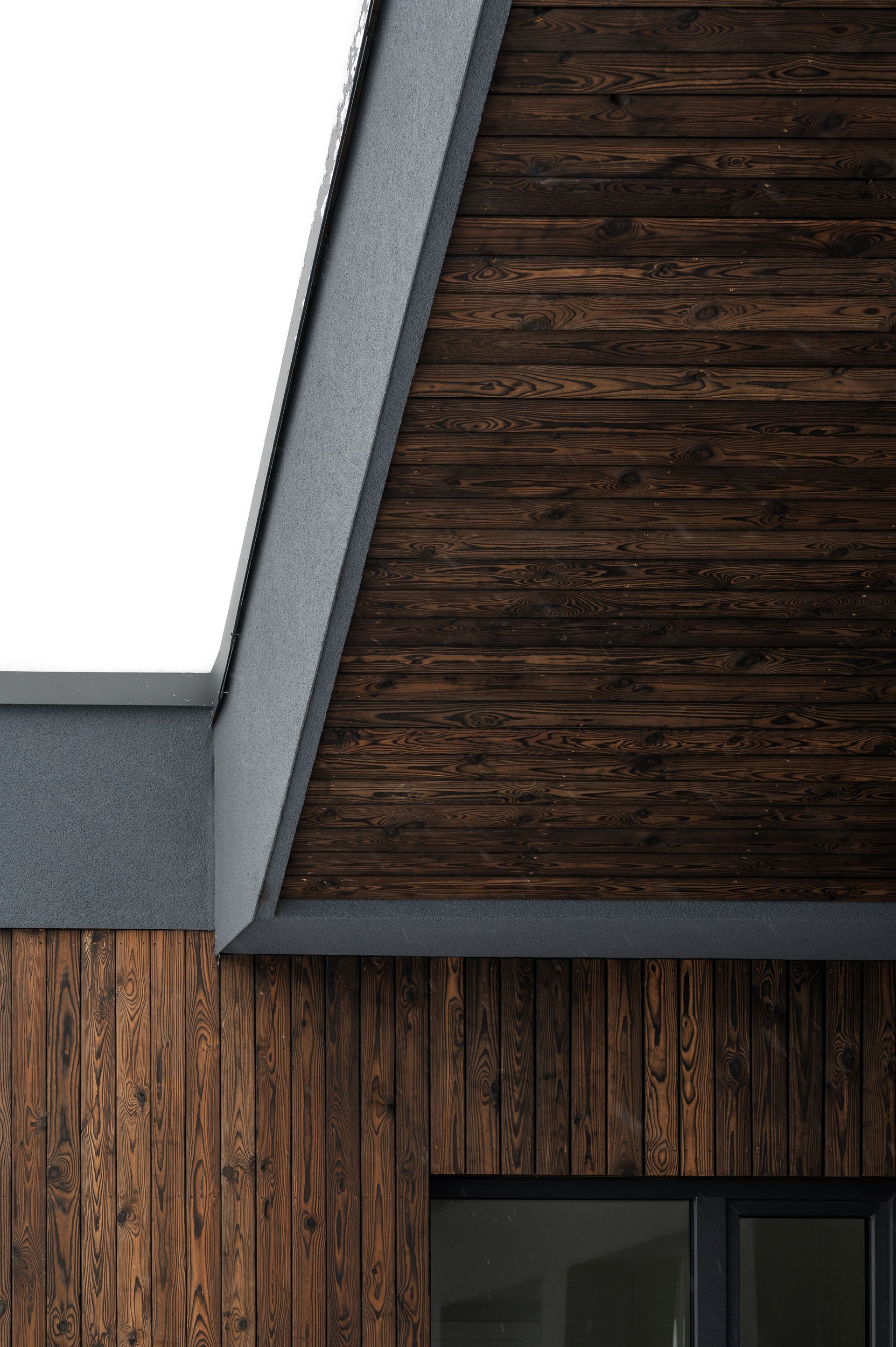 Wooden exterior of a building with a dark roof and concrete trim.