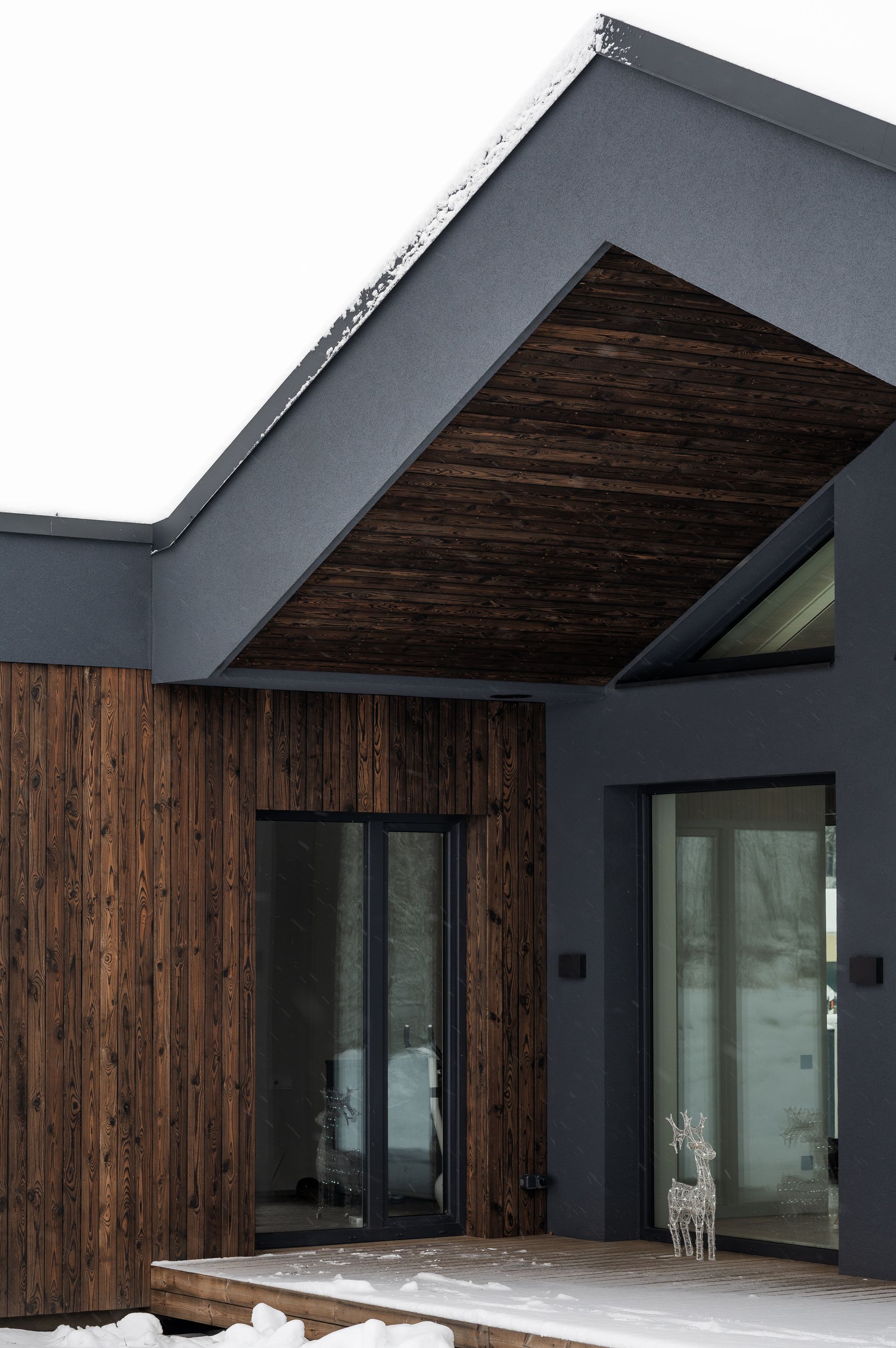 Modern home exterior with gray walls, wood accents, and a snow-covered deck.
