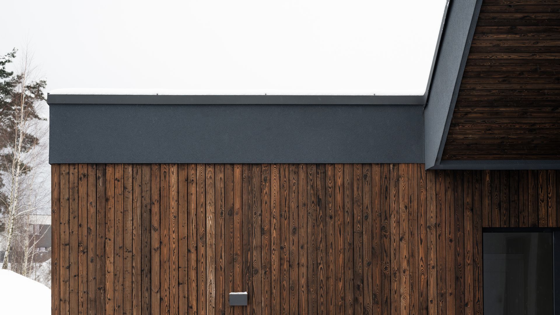 Dark wood siding and dark grey trim on a building with a snowy background.