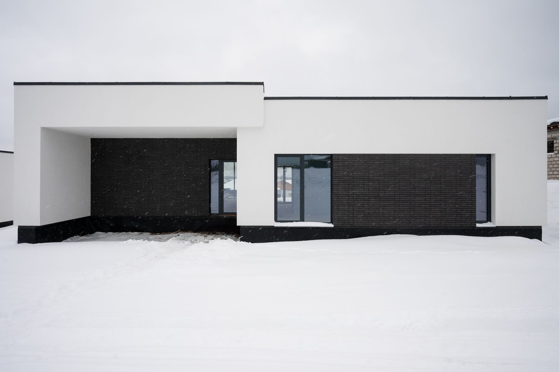 Modern white house with dark accent walls, snowy ground.