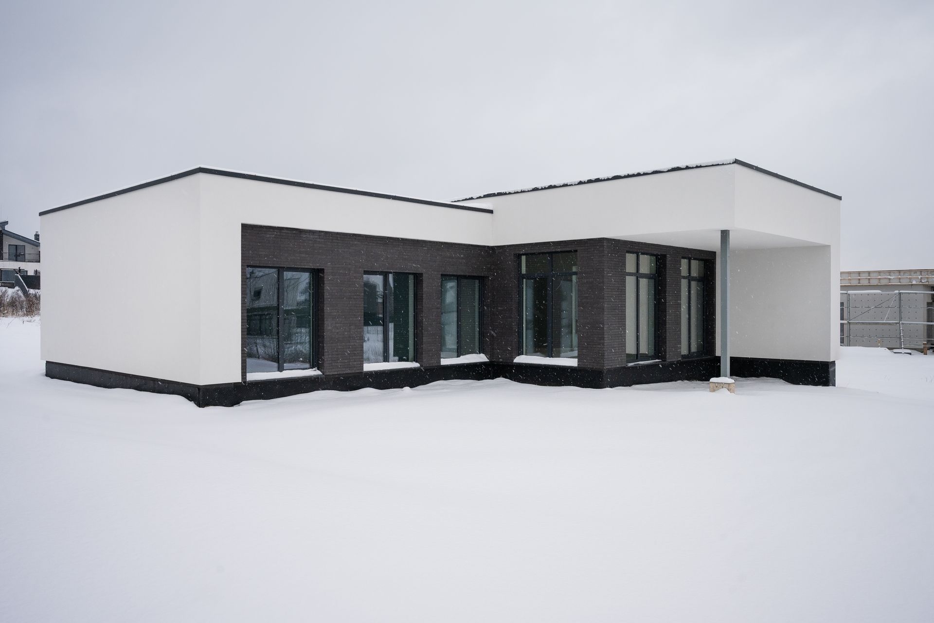 Modern white house with dark brick accents and large windows, surrounded by snow.