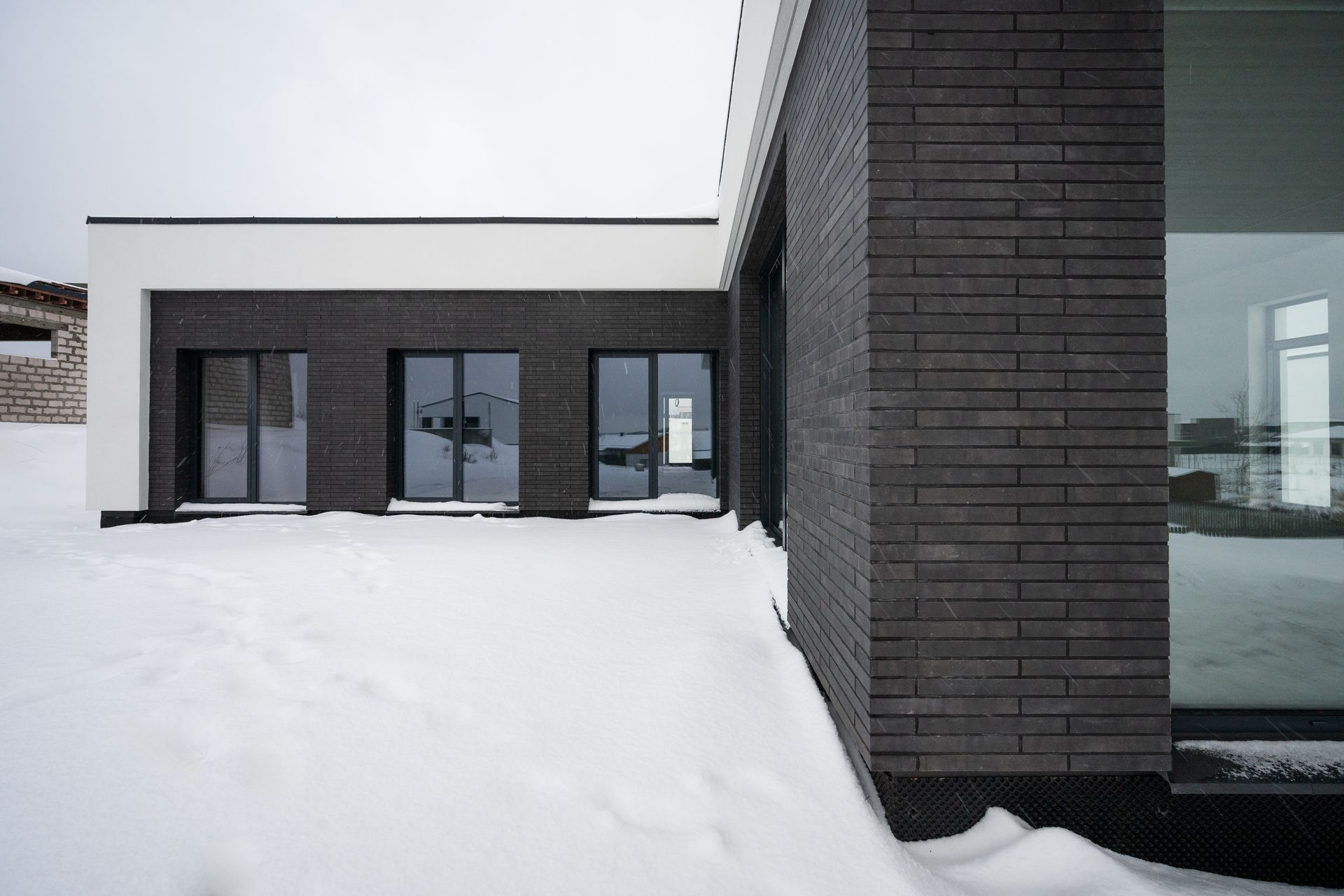 Modern building with dark brick facade, three glass doors, and white roof in a snowy setting.