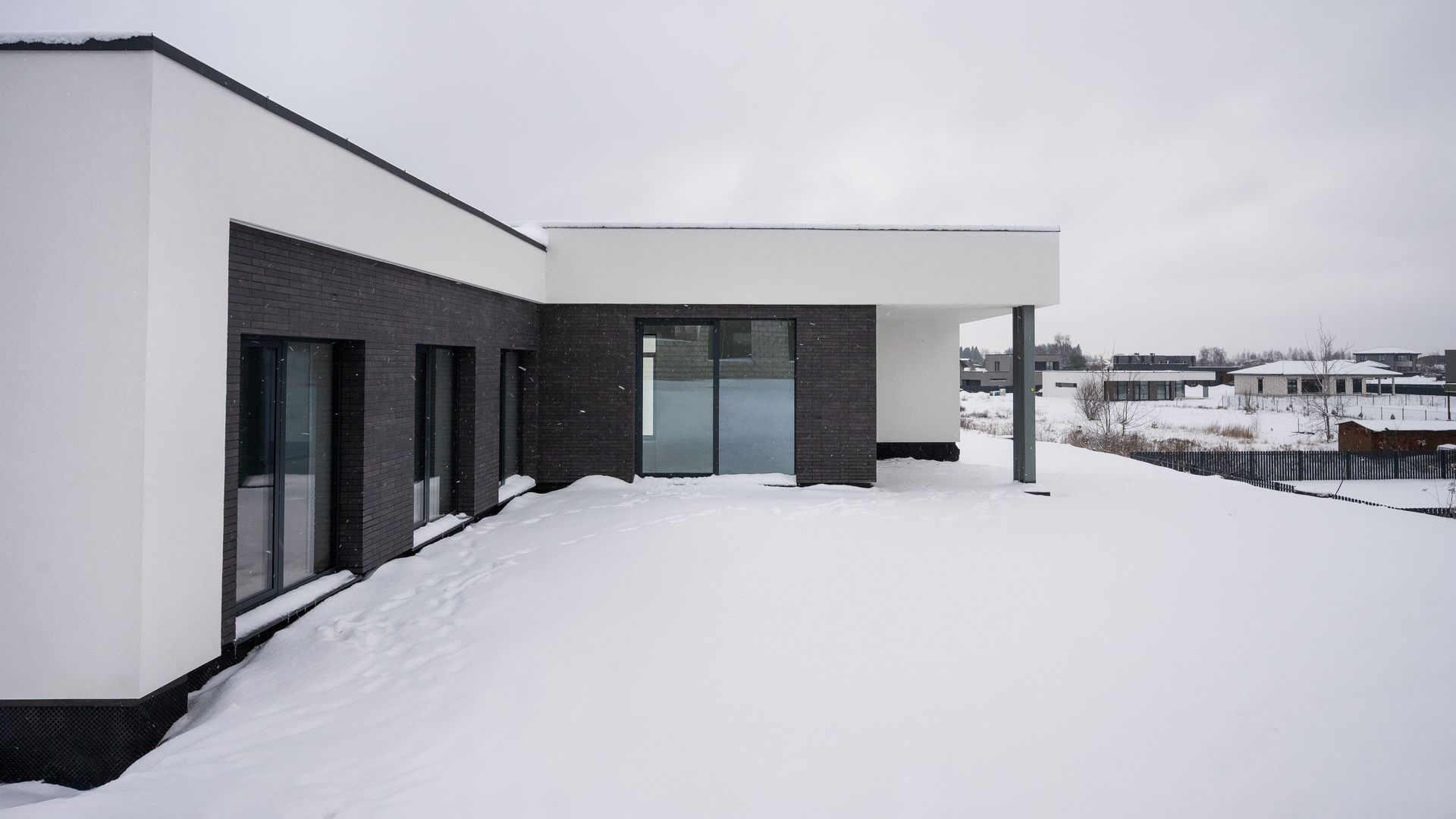 Modern building with white and dark brick facade, covered in snow on a cloudy day.