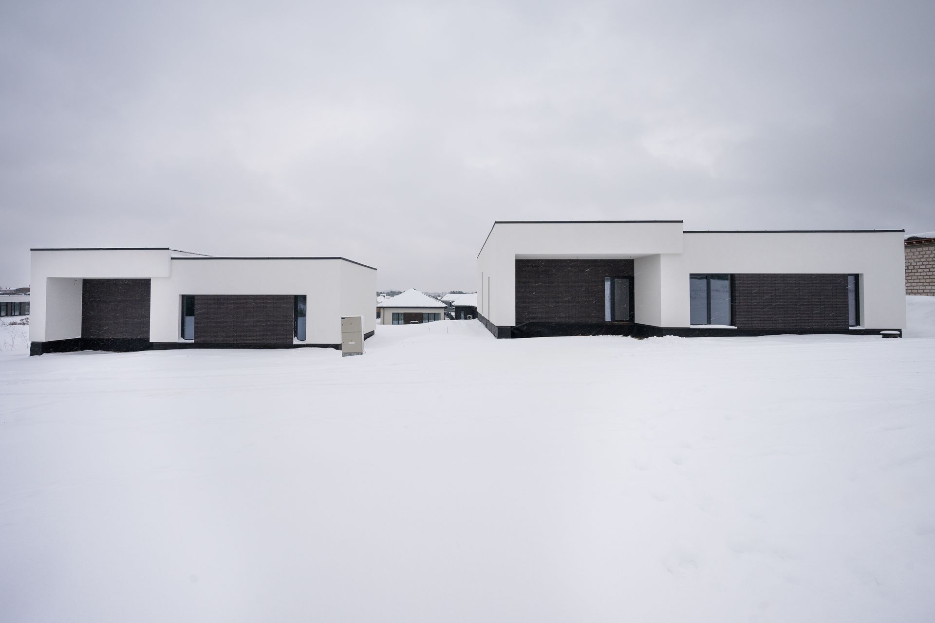 Modern white houses with dark brick accents in a snowy landscape.
