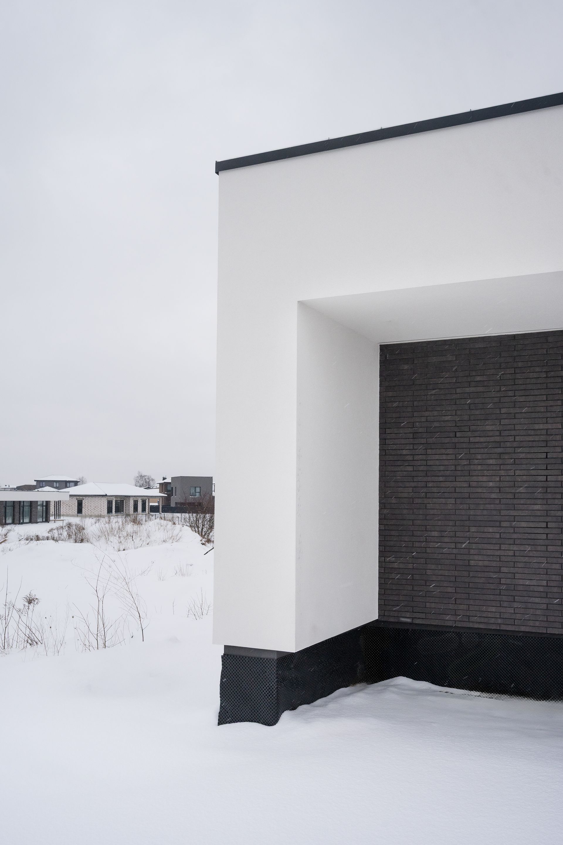 Corner of a modern white building with dark brick facade in a snowy landscape.