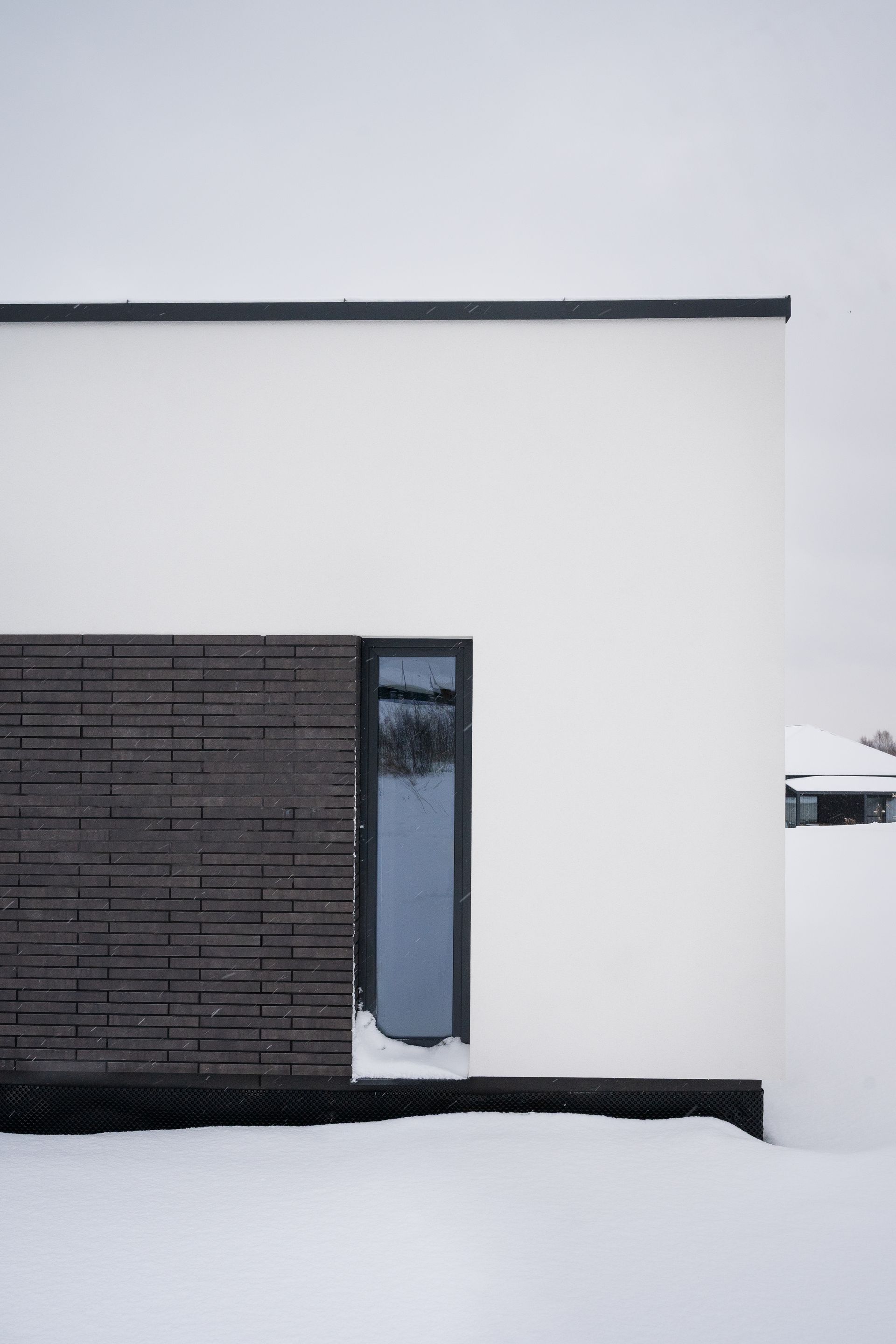 White modern building corner with dark wood paneling, narrow window, and snow.