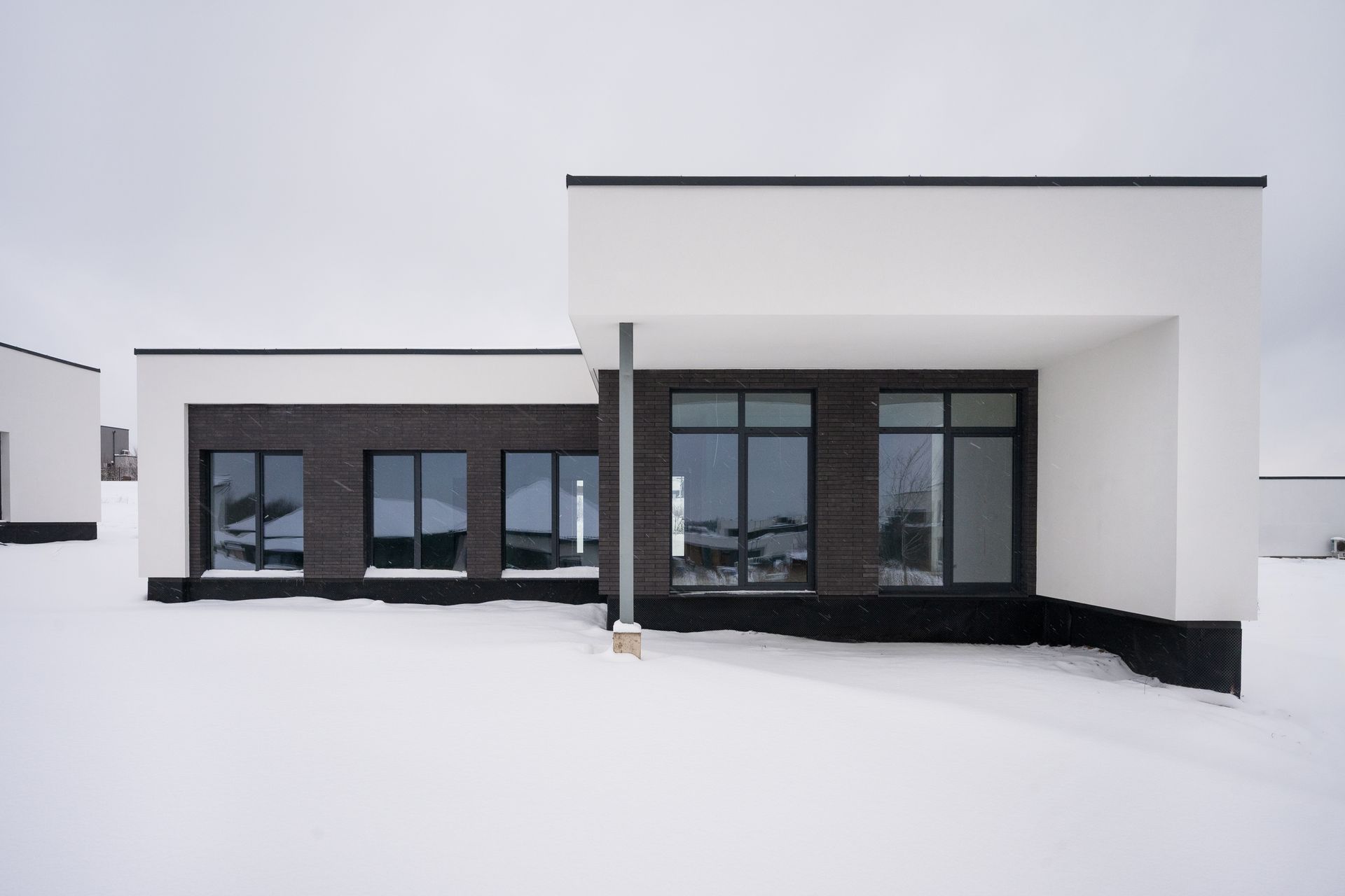 Modern house with white and dark brick exterior in snowy landscape.