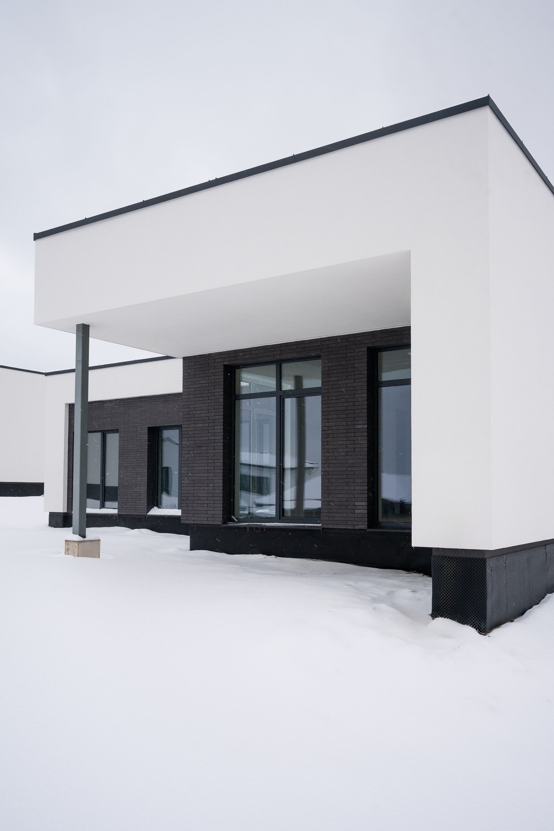 Modern white and black building with snow-covered ground; covered entrance.