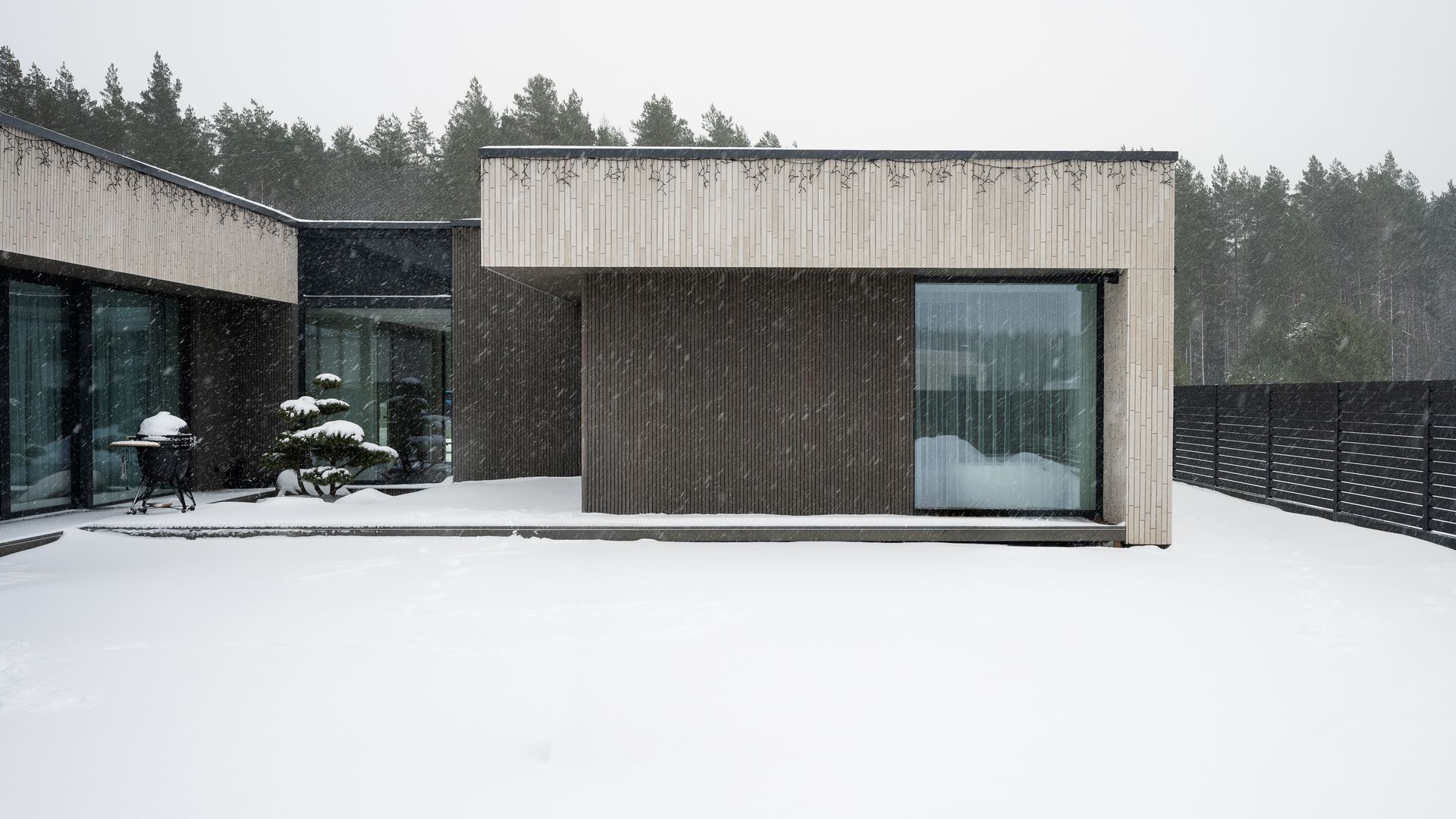 Modern house in a snowy forest. Snow covers the ground and falls on the building.