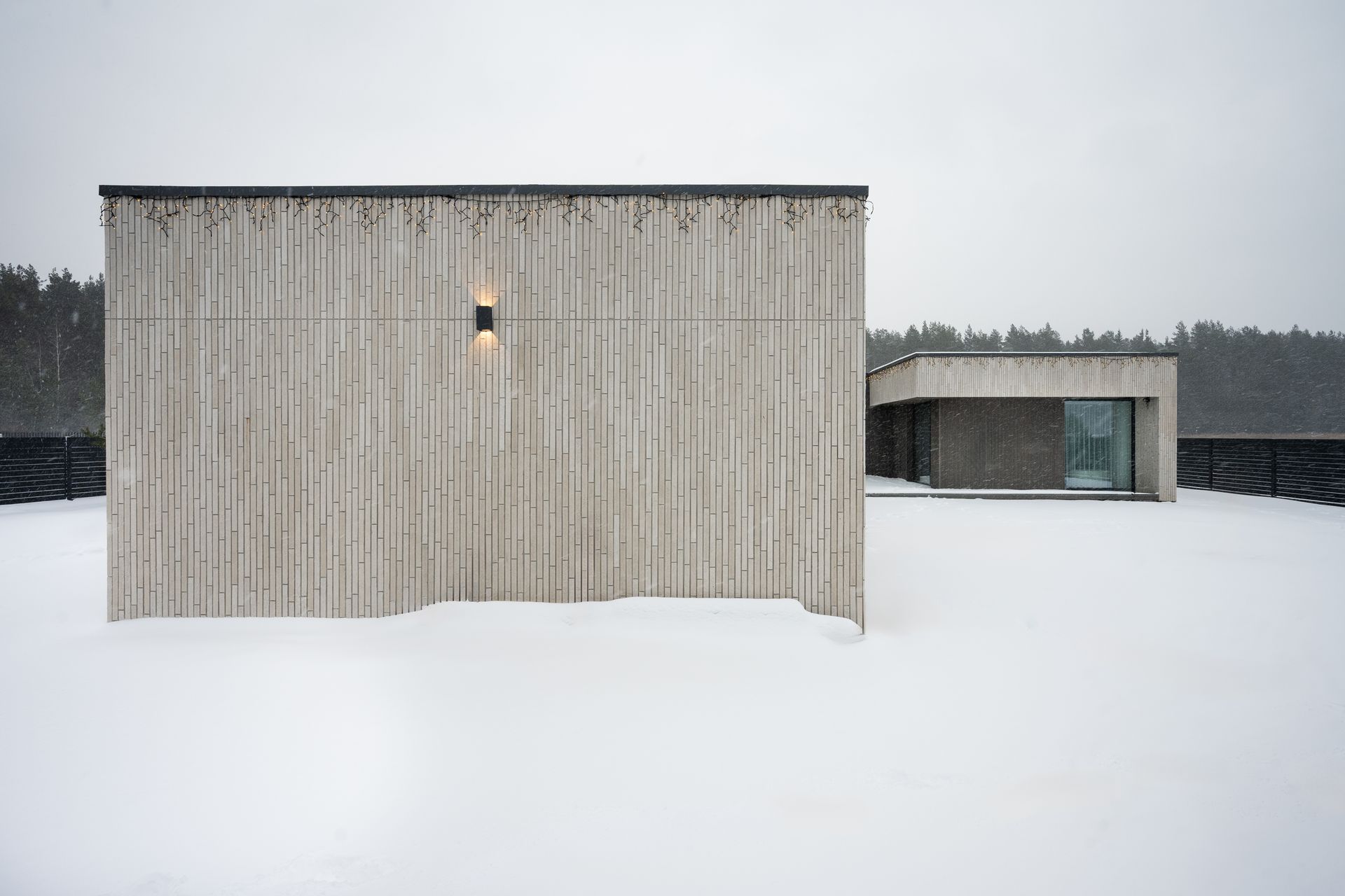 Two modern buildings with vertical wooden siding in a snowy landscape. One building has a light.