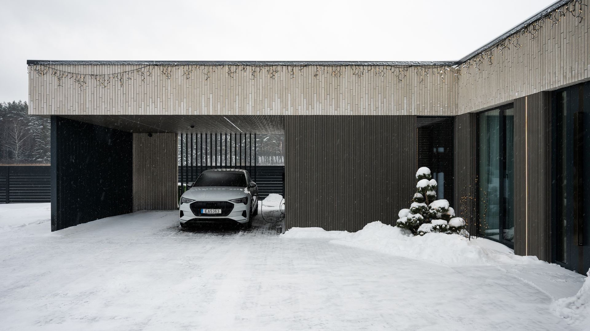 White car parked under a carport, snow on the ground, modern house exterior.