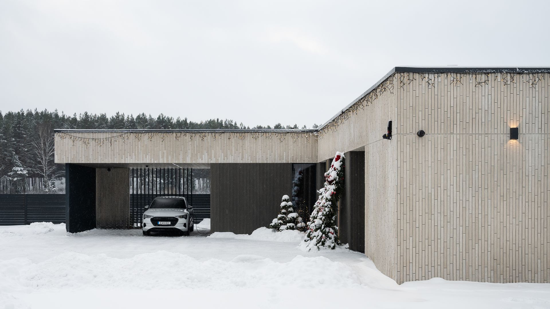 Modern house with a car parked under a carport in a snowy setting.