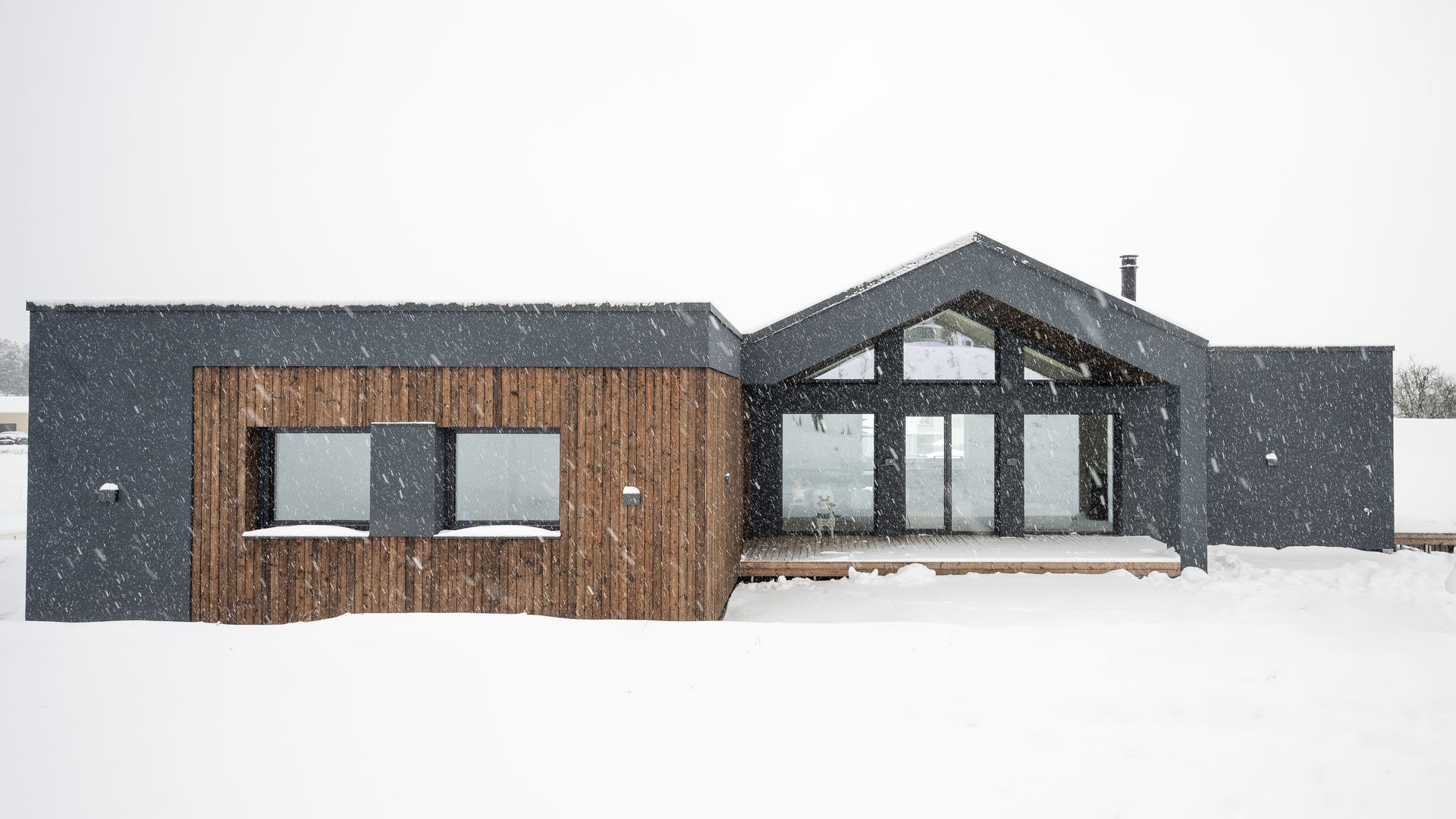 Modern house with a dark facade and wooden accents in a snowy field.