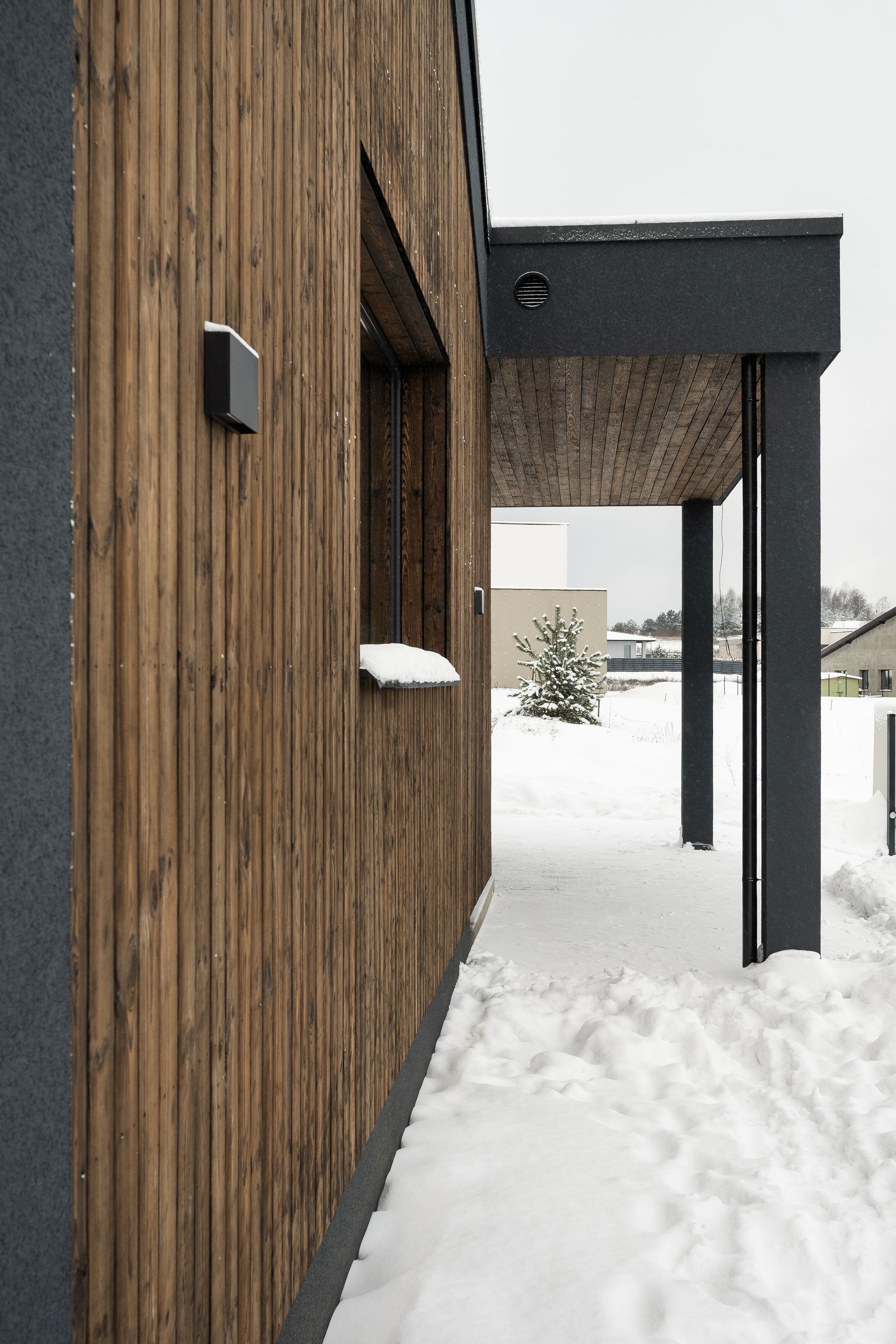 Wooden building exterior with a snow-covered porch. Dark grey trim and vertical wood siding.