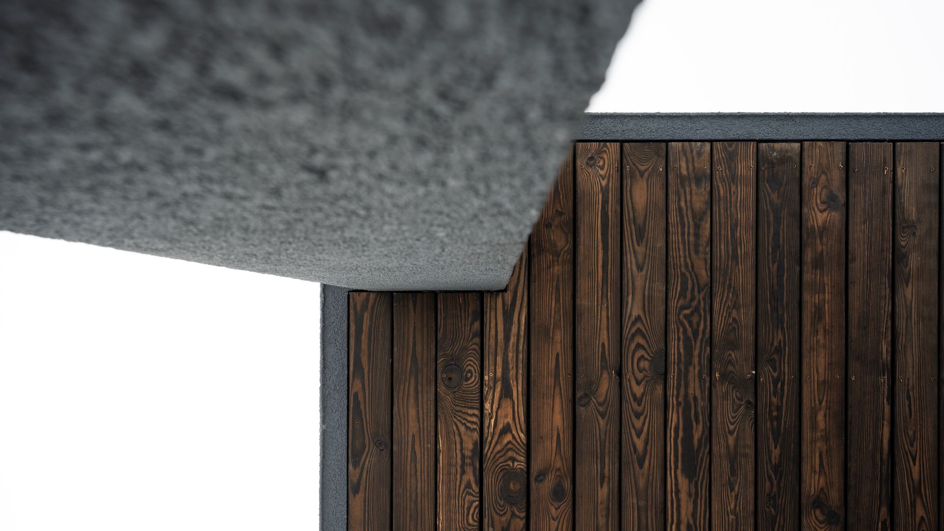 Dark wooden wall next to a textured gray concrete overhang, white background.