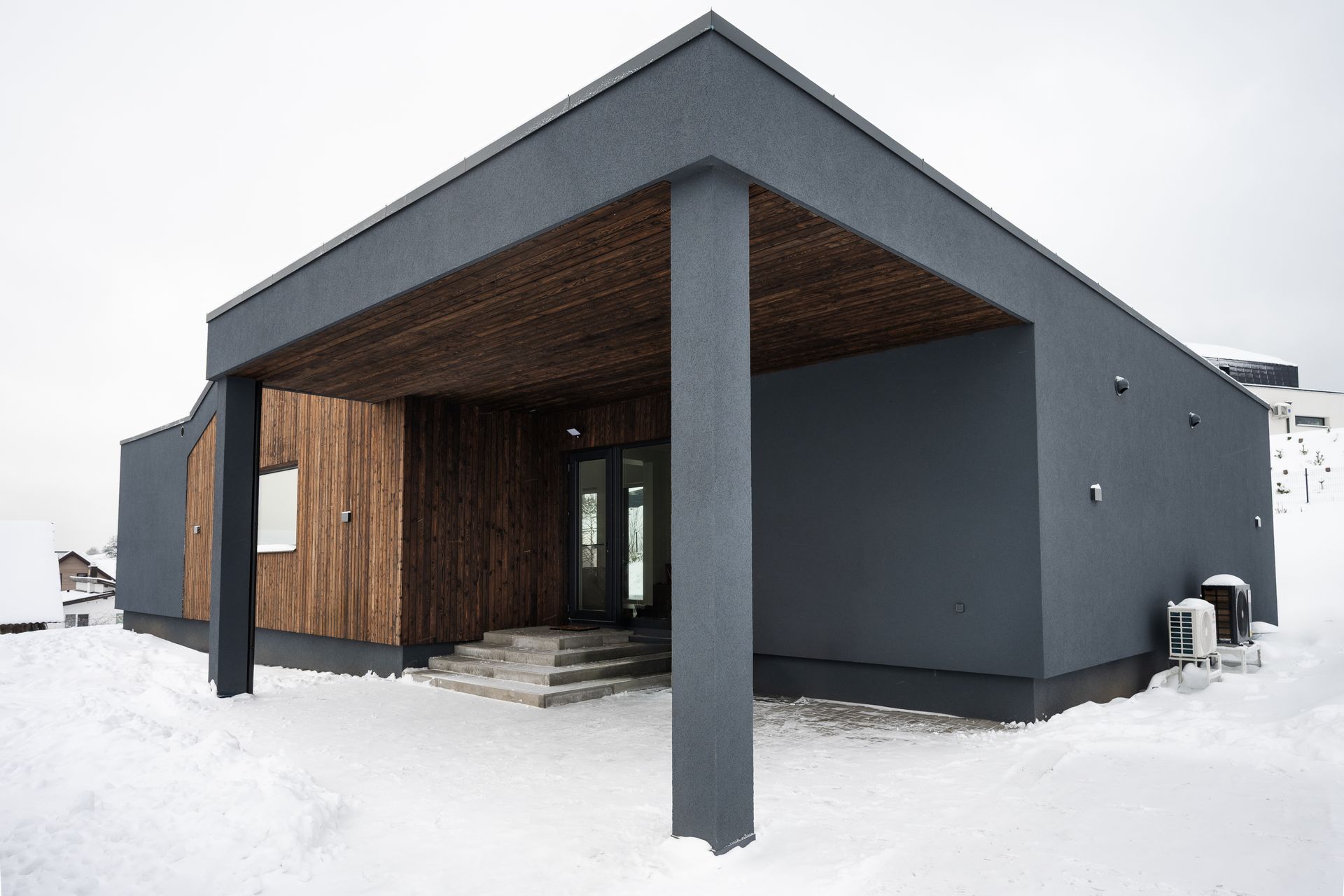 Modern gray building with wooden accents, snow-covered ground, covered entrance.