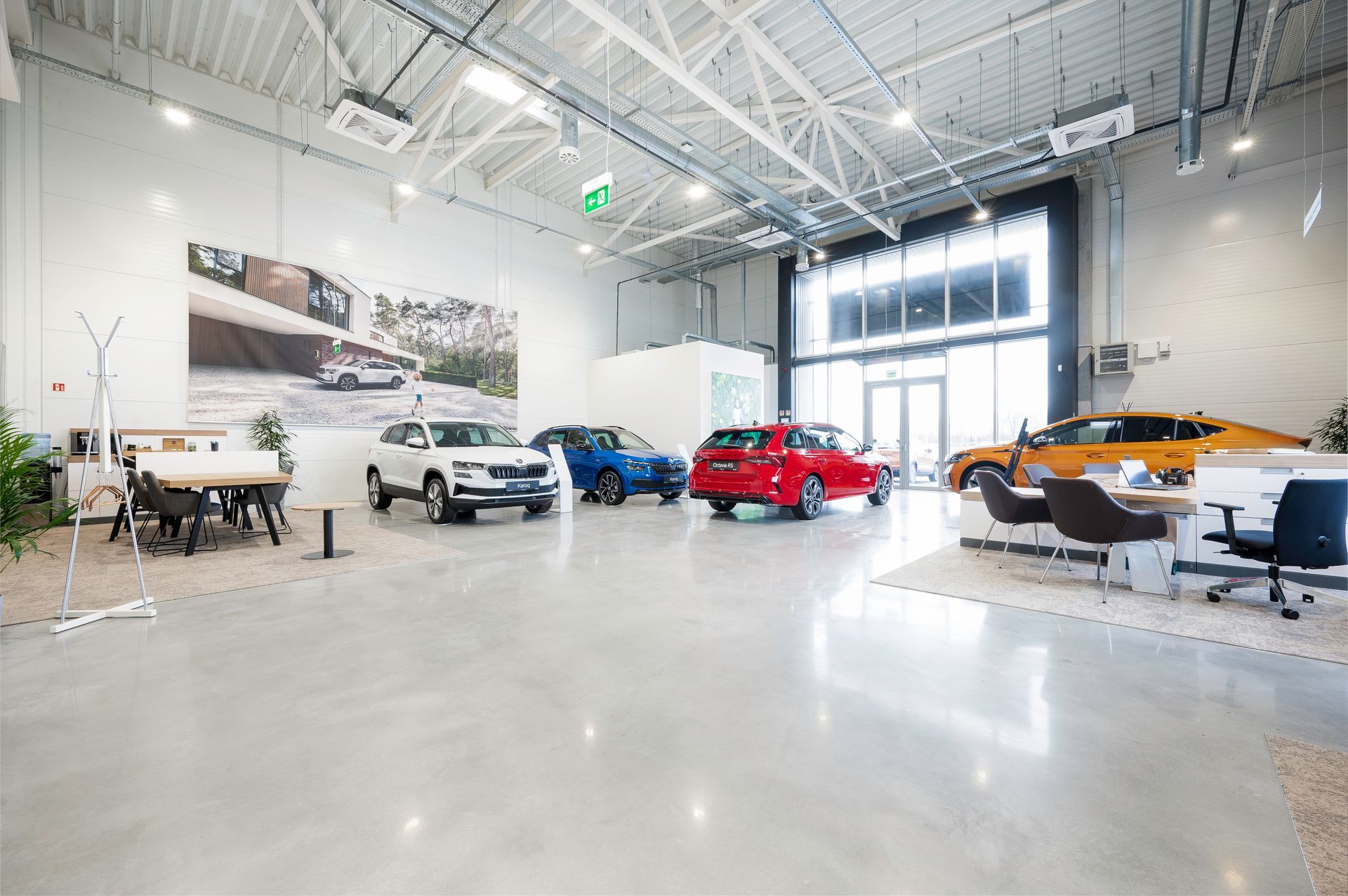 Didelis salonas, pilnas automobilių, stalų ir kėdžių.