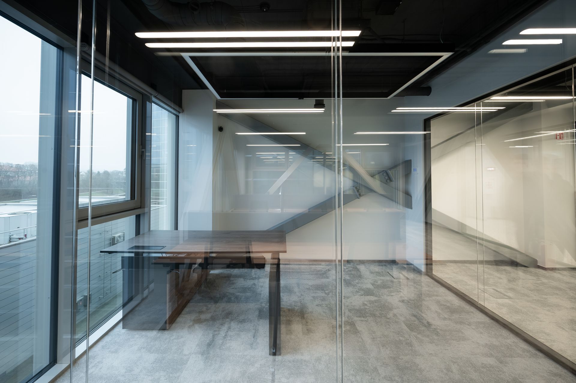 Modern office space with a desk by a large window, glass walls, and a staircase in the background.