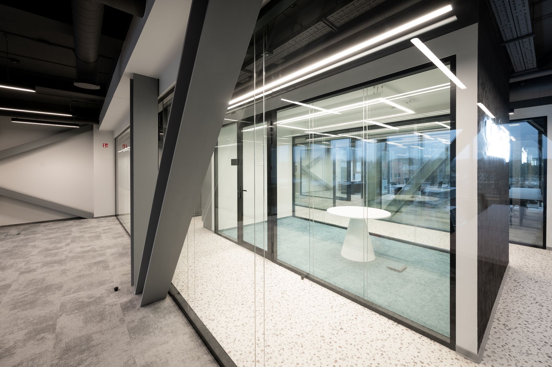 Modern office interior with glass-walled meeting room, gray structural beams, and a white round table.