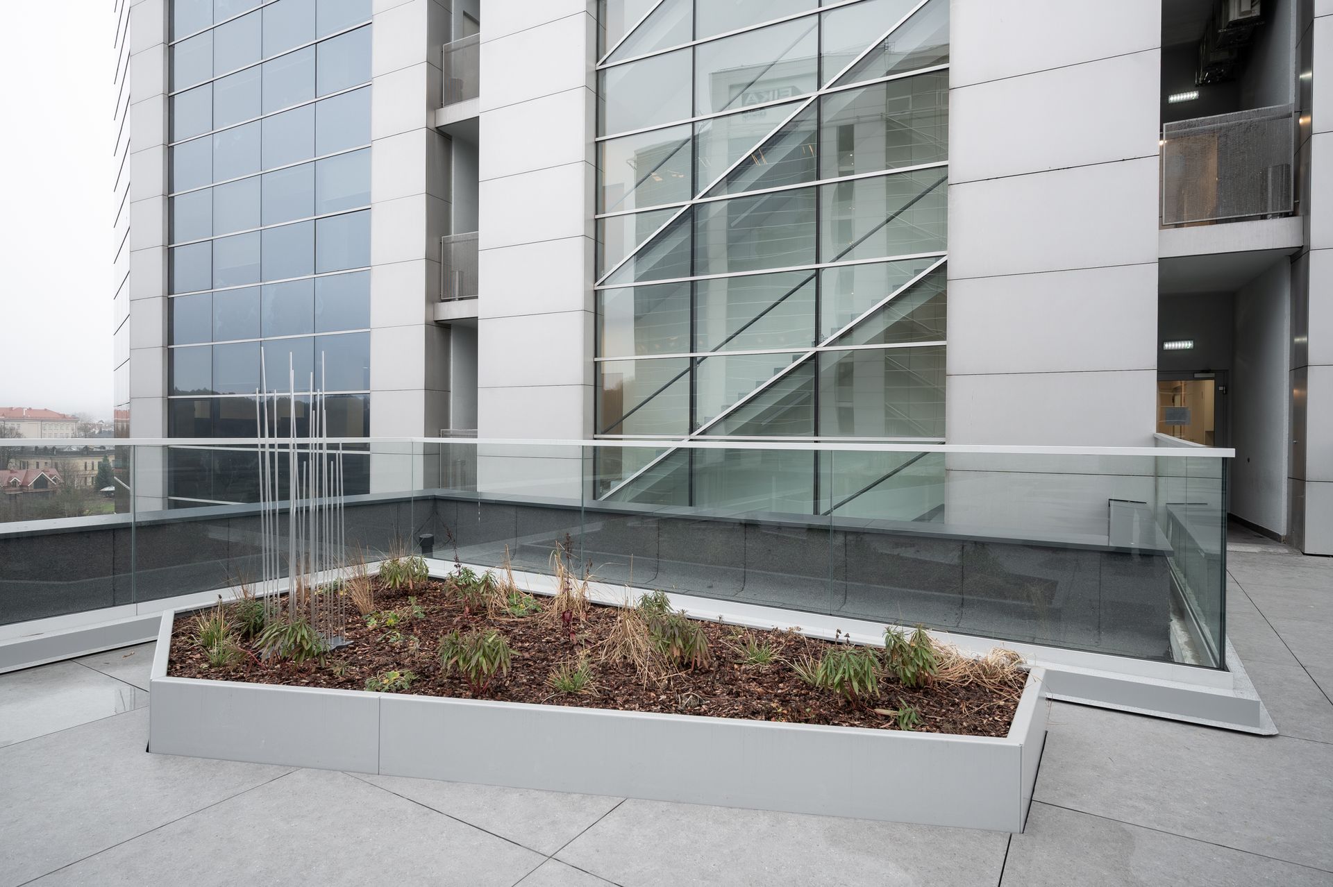 Rooftop garden with glass railing, modern building exterior, overcast sky.