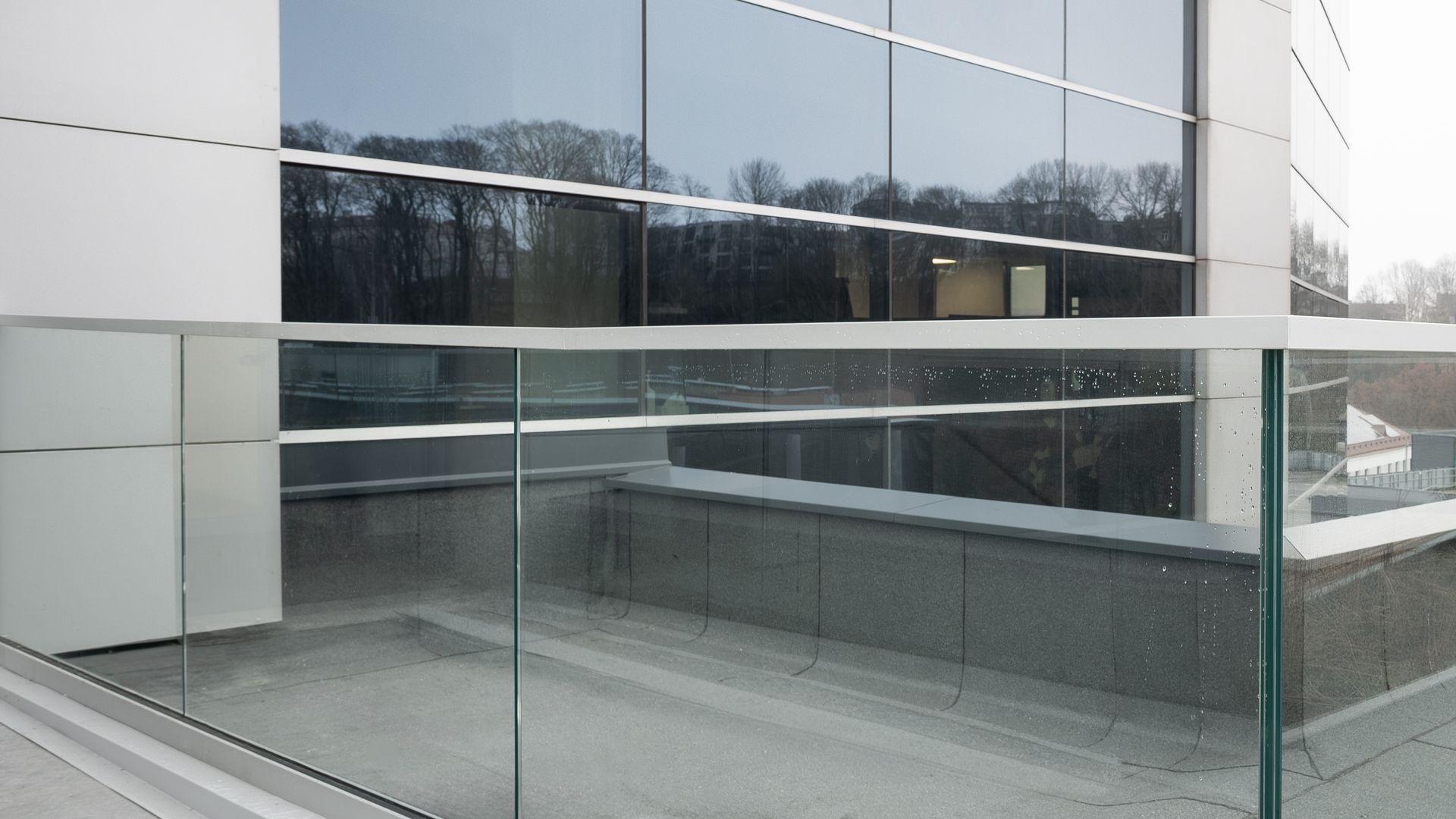 Modern building with glass walls reflecting trees and a clear glass balcony railing.