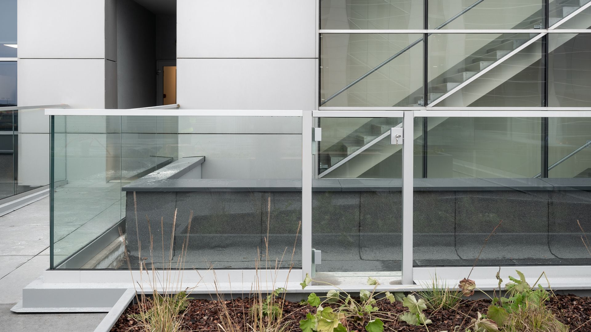 Exterior of a modern building with a glass railing, stairs visible through a window, and a planter box.