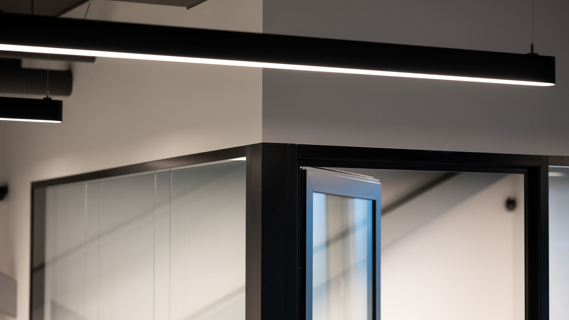 Black rectangular overhead light in modern office setting, casting light on glass partition.