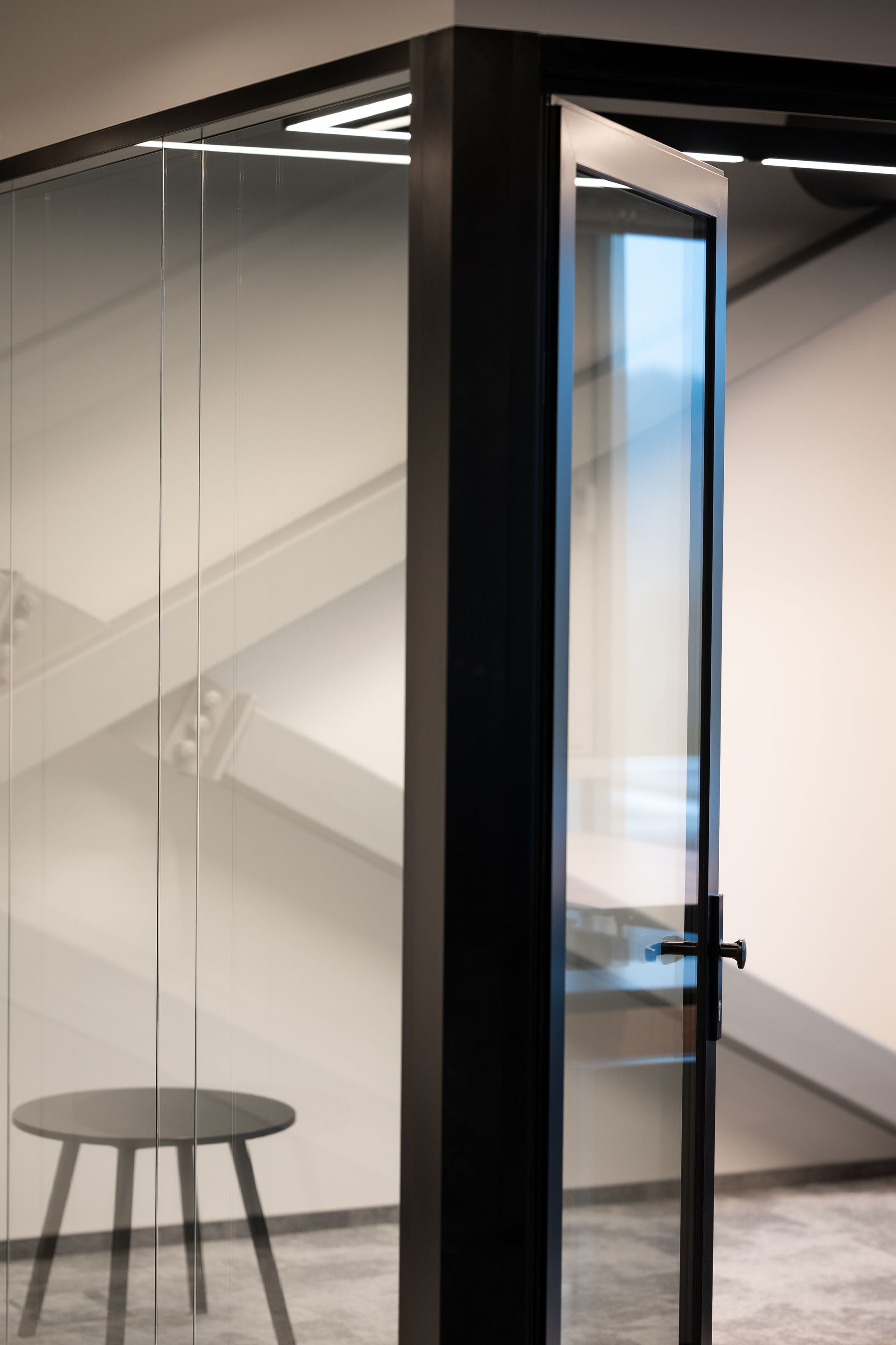 Glass office partition with black frame and open door; small table visible.