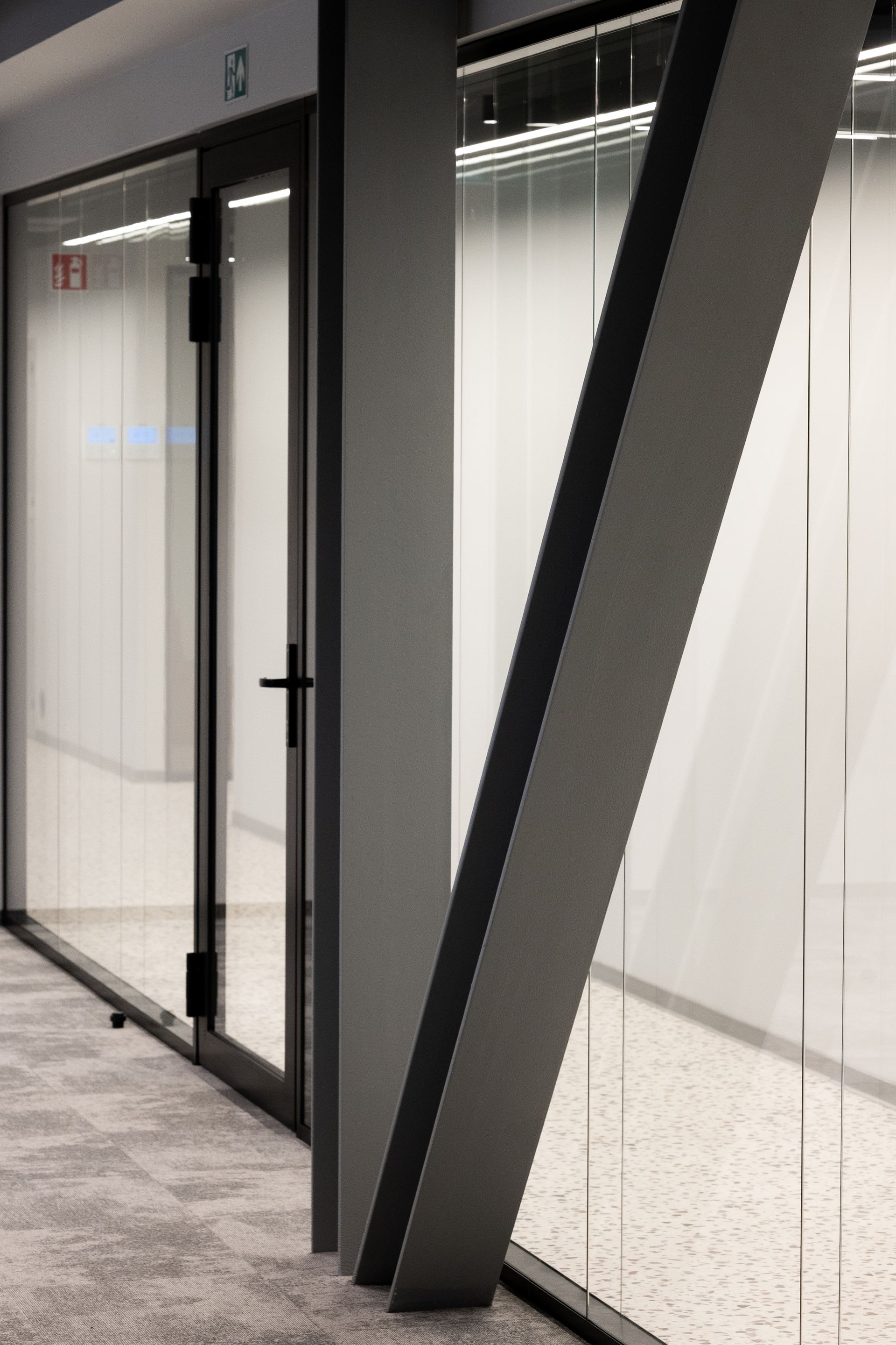 Interior view of a modern office hallway with glass walls and a diagonal support beam.