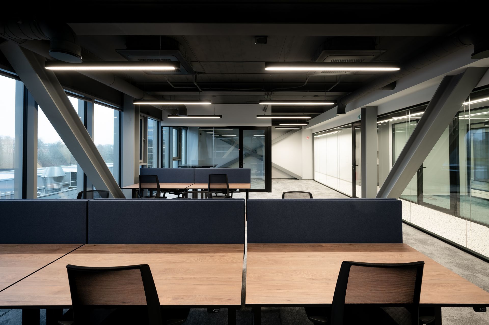 Modern office interior with workstations, large windows, and exposed steel beams.