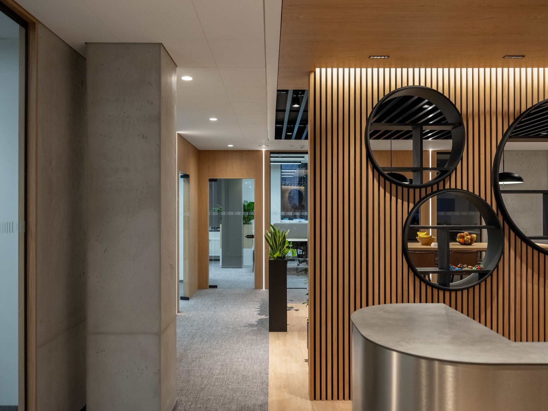 Vestibiulis su nerūdijančio plieno prekystaliu ir trimis apvaliais veidrodžiais ant sienos.