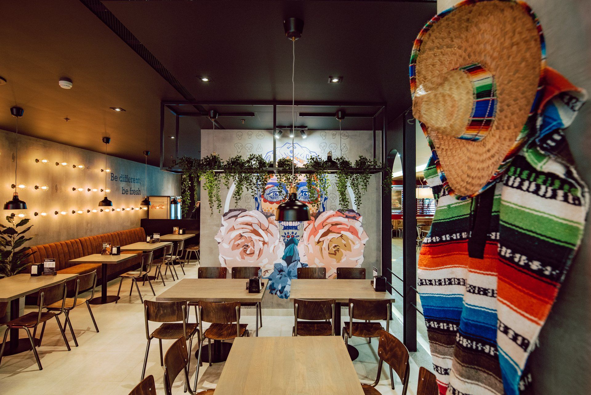 Restoranas su stalais, kėdėmis ir sombrero ant sienos.