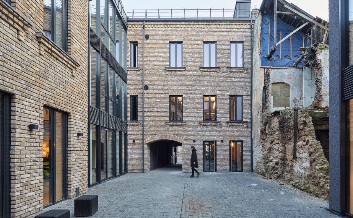 Vyras eina akmenimis grįsta gatve priešais plytų pastatą.