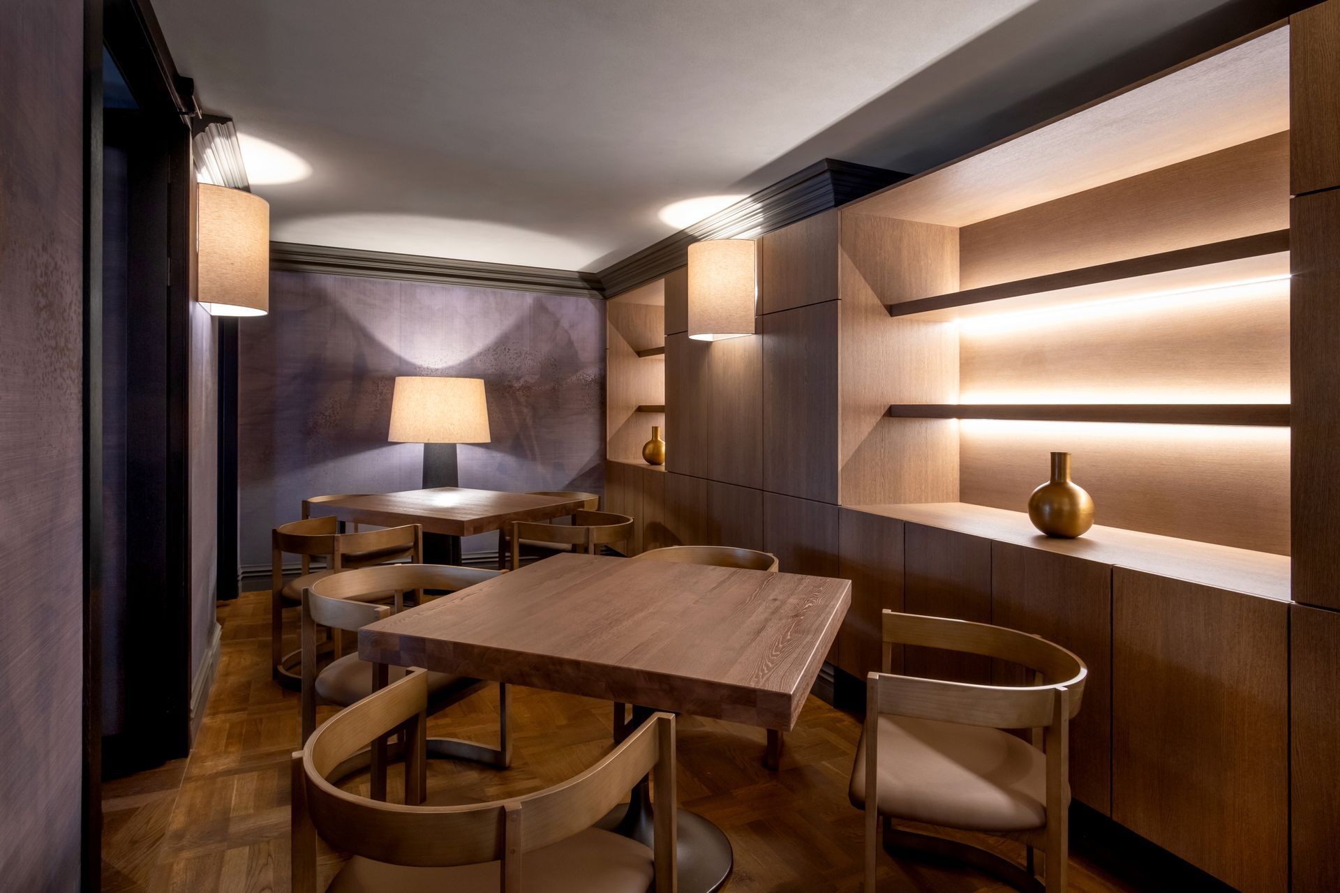 Kambarys su stalais, kėdėmis ir lempa ant sienos.