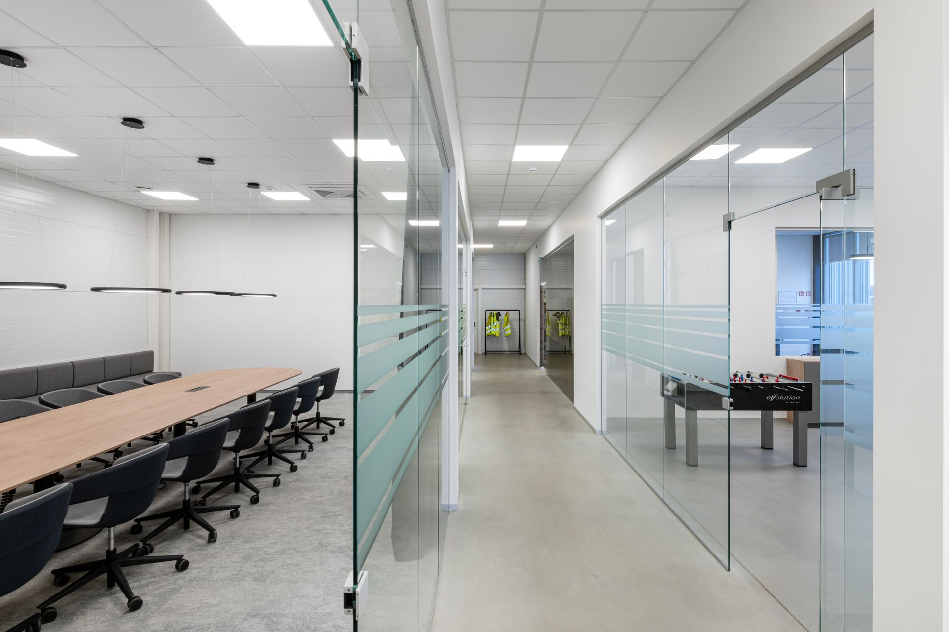 Ilgas koridorius biurų pastate su stalu ir kėdėmis.