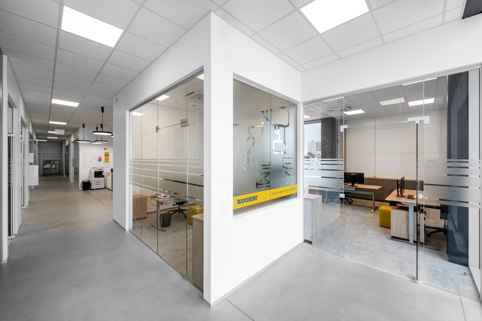 Koridorius biurų pastate su stiklinėmis durimis tarp dviejų kambarių.