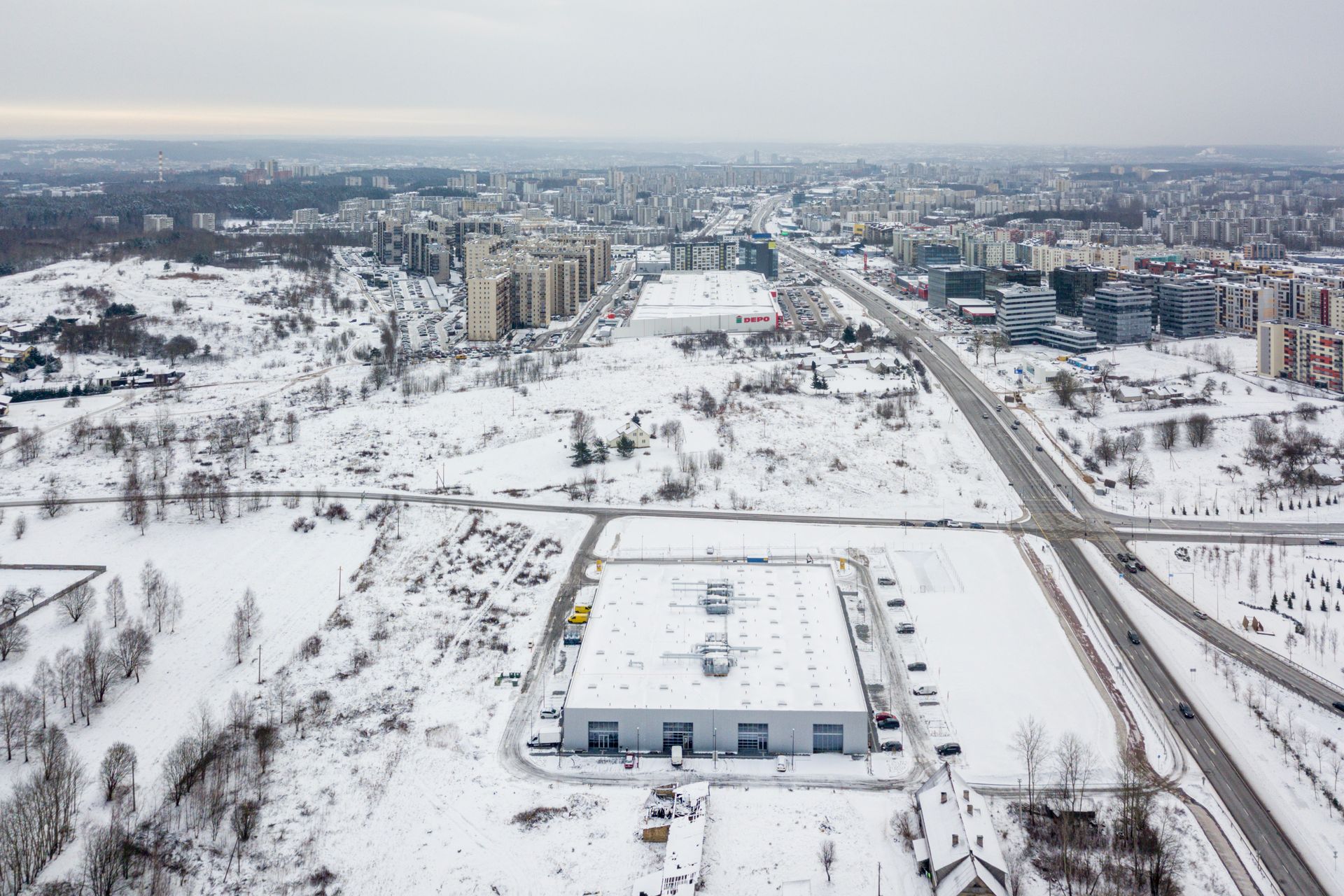 Snieguoto miesto vaizdas iš oro su dideliu pastatu viduryje.