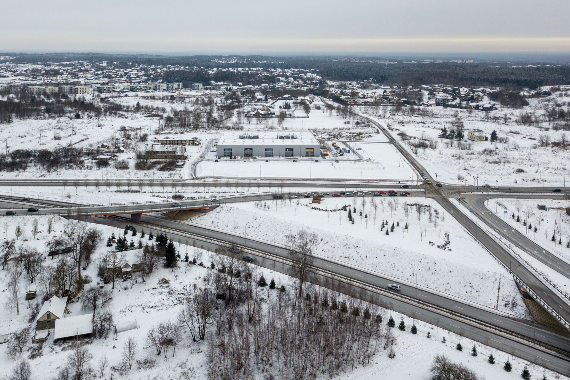 Snieguoto kraštovaizdžio vaizdas iš oro su greitkeliu priekiniame plane.