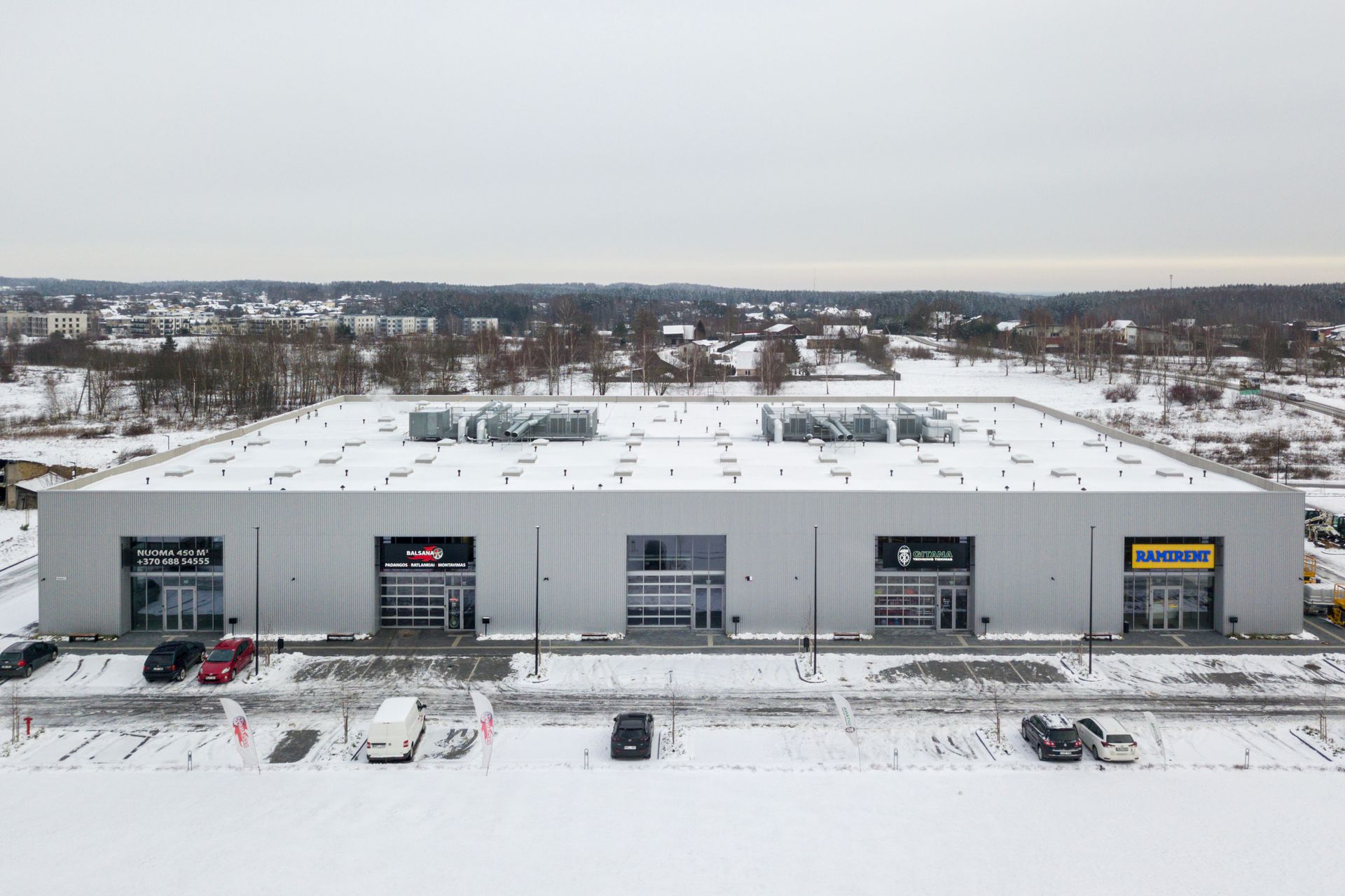 Iš oro vaizdas, kuriame matomas didelis pastatas sniege ir priešais jį pastatyti automobiliai.