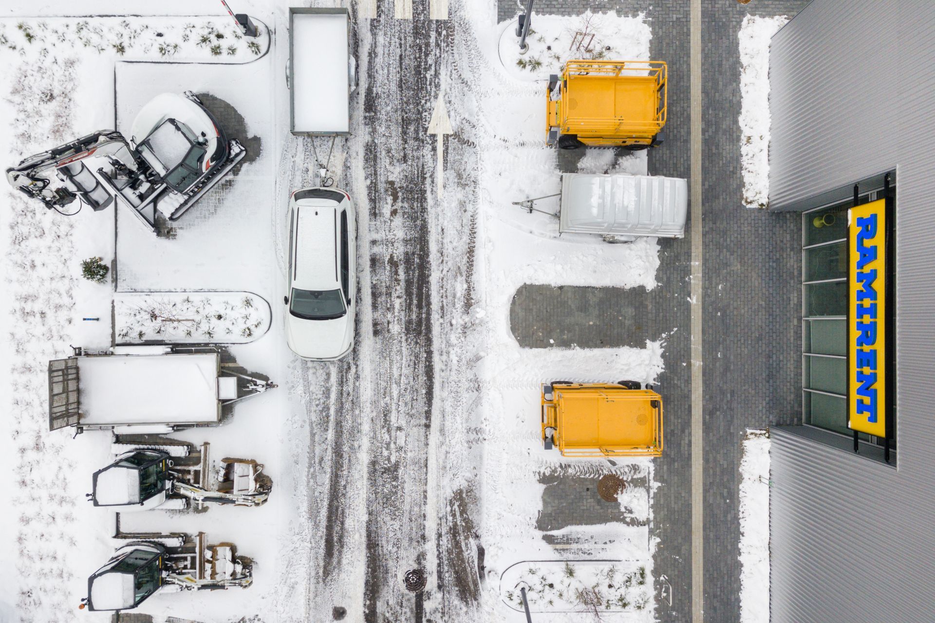 Vaizdas iš oro, kuriame matyti automobilių stovėjimo aikštelė su sunkvežimiais, pastatytais priešais pastatą su užrašu „maskin“