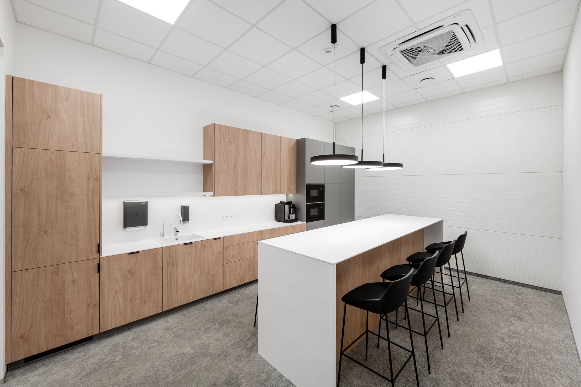 Virtuvė su medinėmis spintelėmis, didele sala ir taburetėmis.