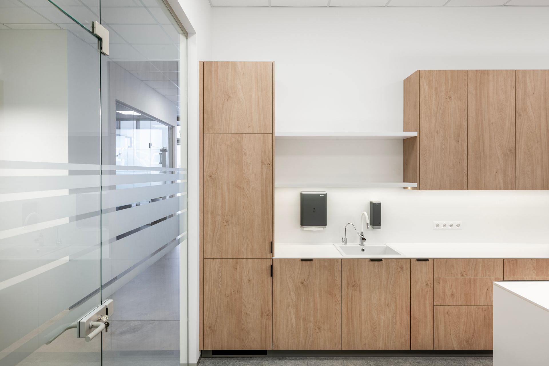 Virtuvė su medinėmis spintelėmis, kriaukle ir stiklinėmis durimis.