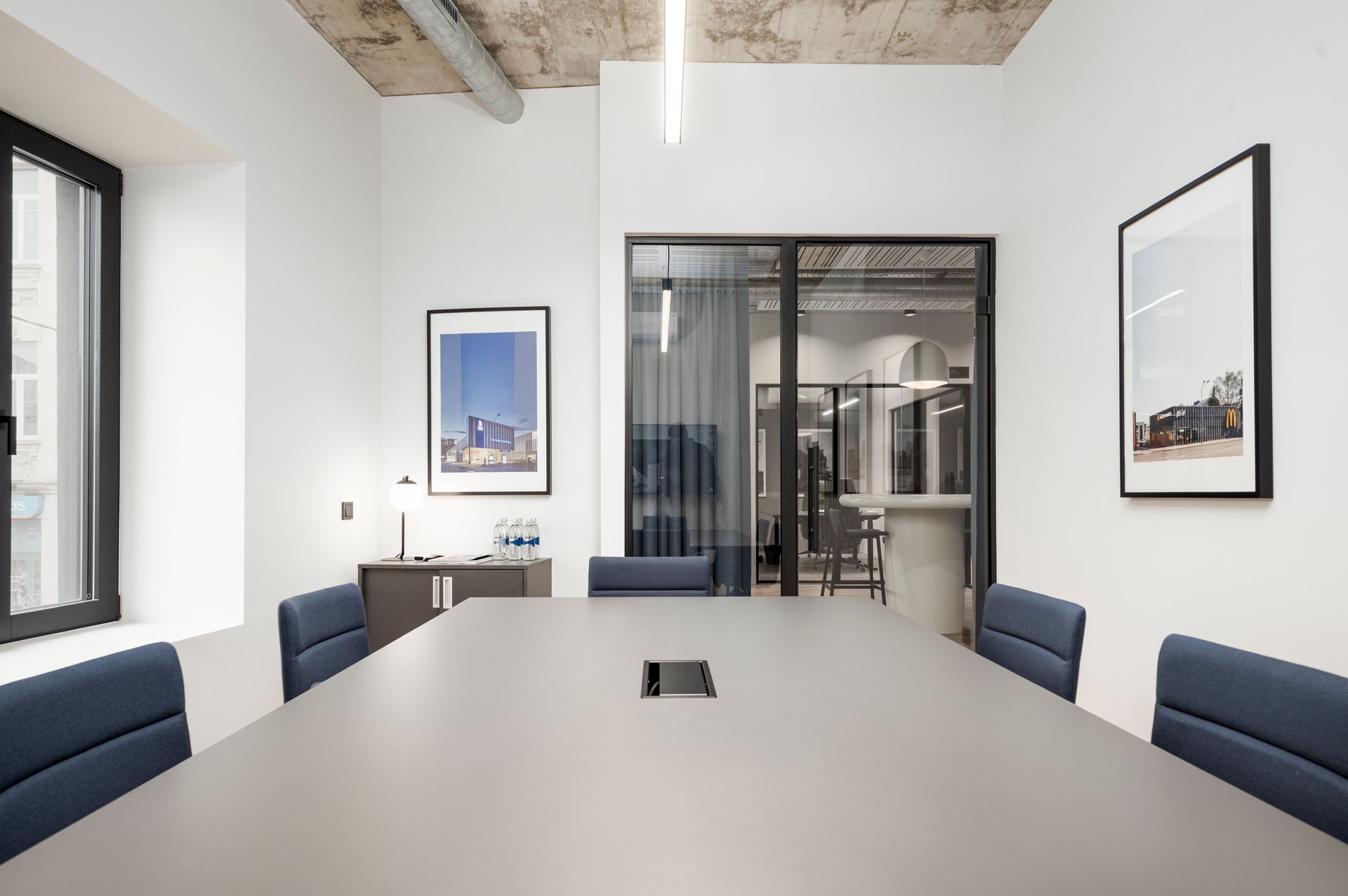 Konferencijų salė su ilgu stalu ir mėlynomis kėdėmis.