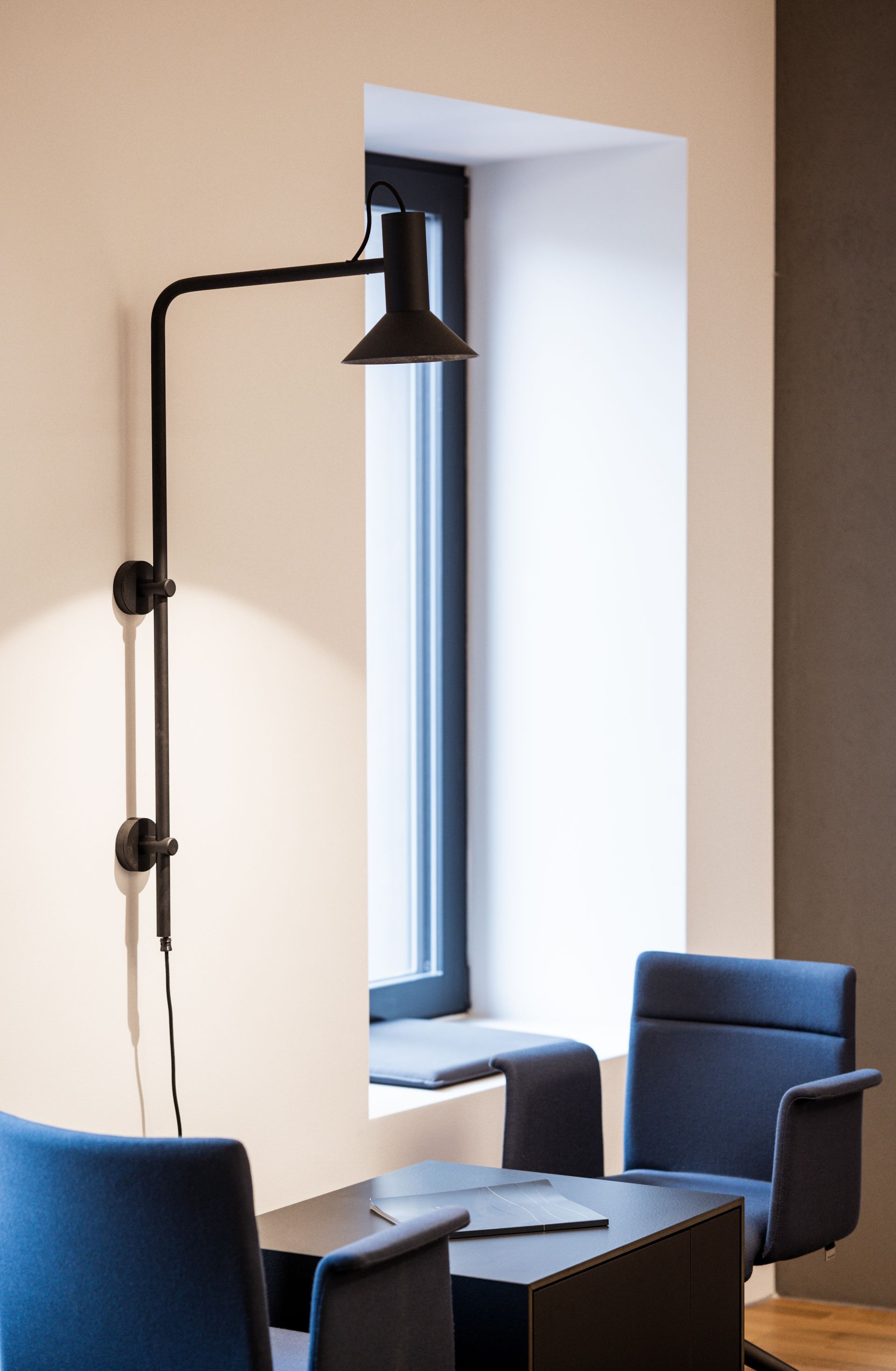 Kambarys su stalu, kėdėmis ir lempa ant sienos.